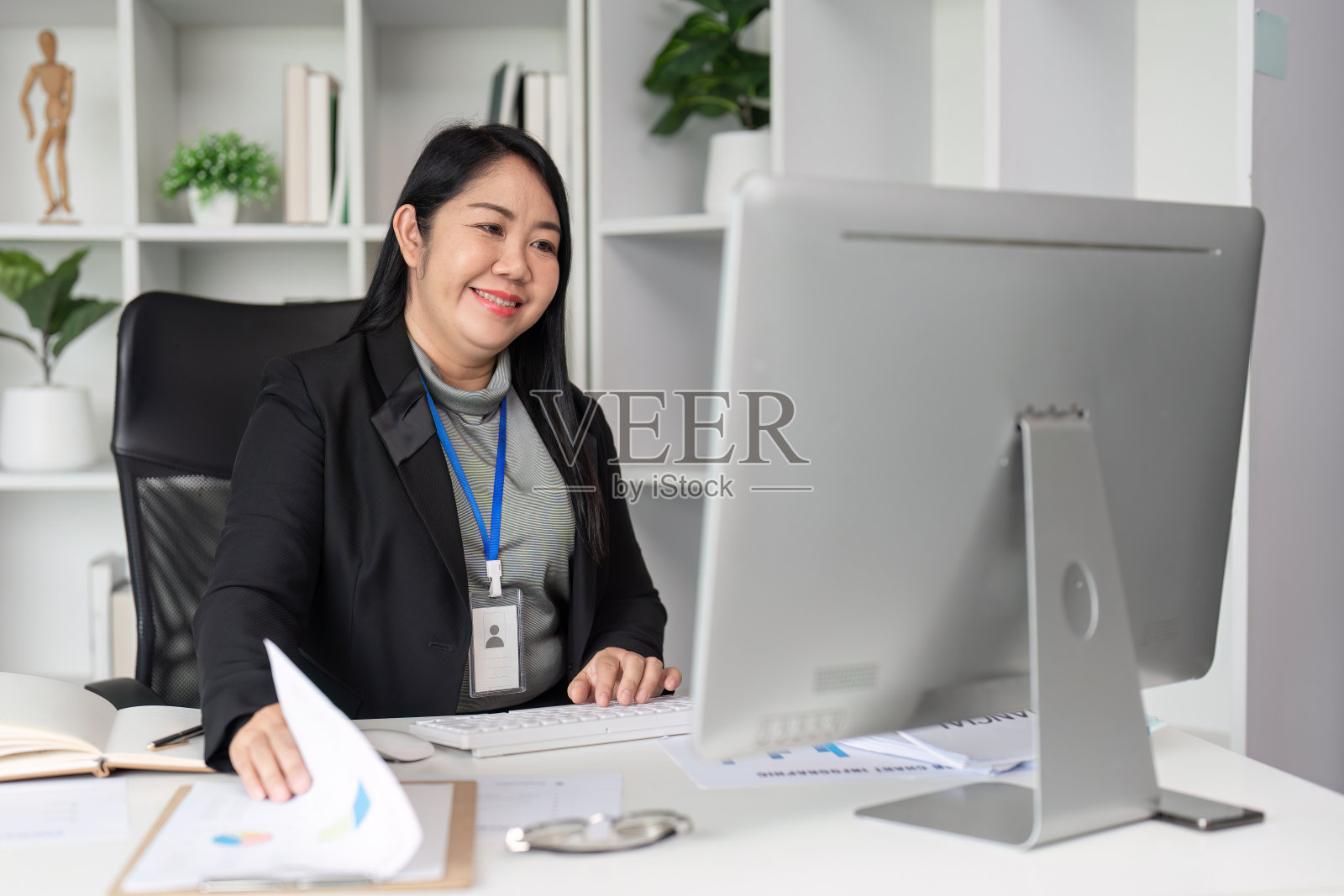 中年女商人在现代办公环境中使用电脑和文件处理文书工作照片摄影图片