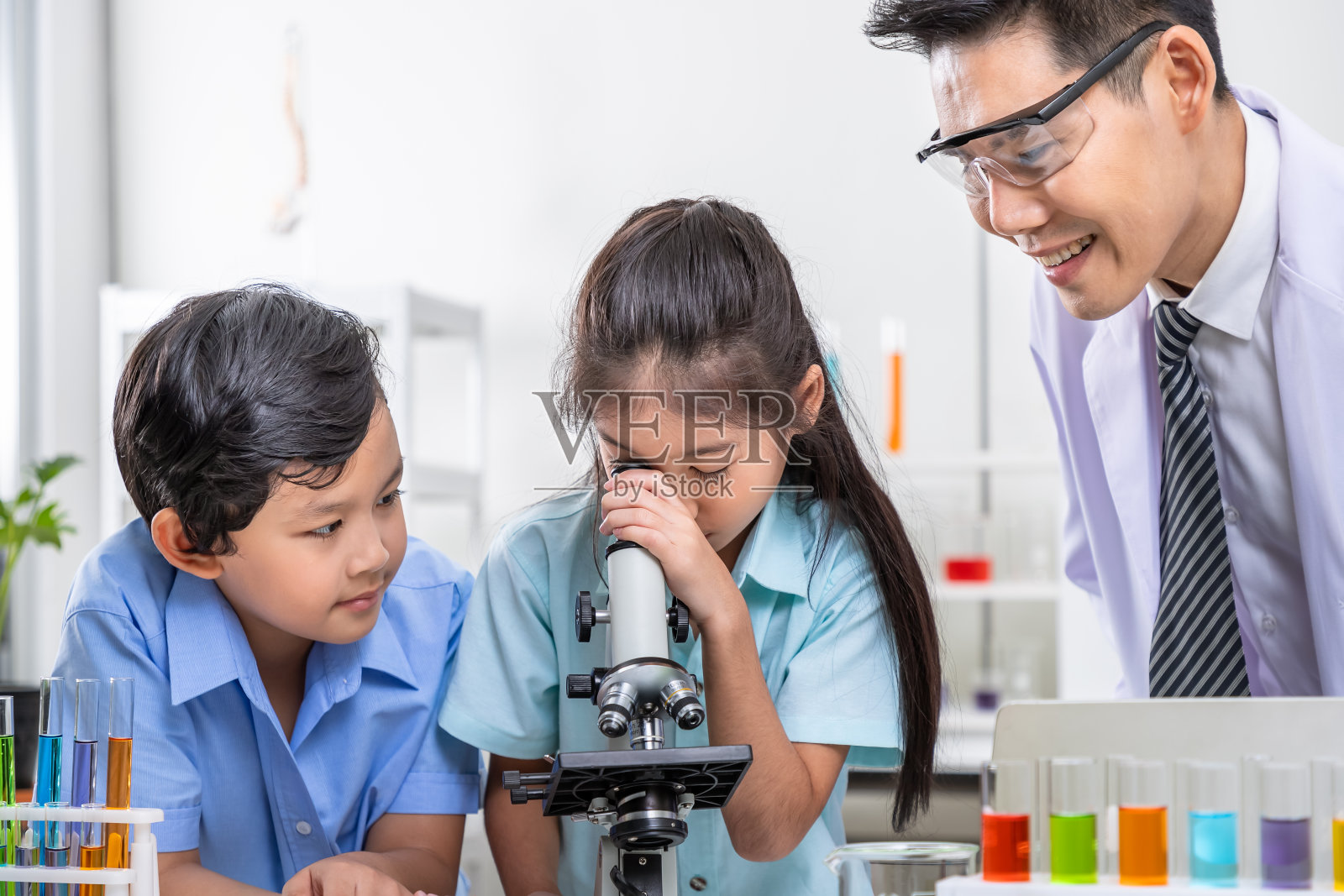 亚洲小学生在老师的带领下,用显微镜探索科学照片摄影图片