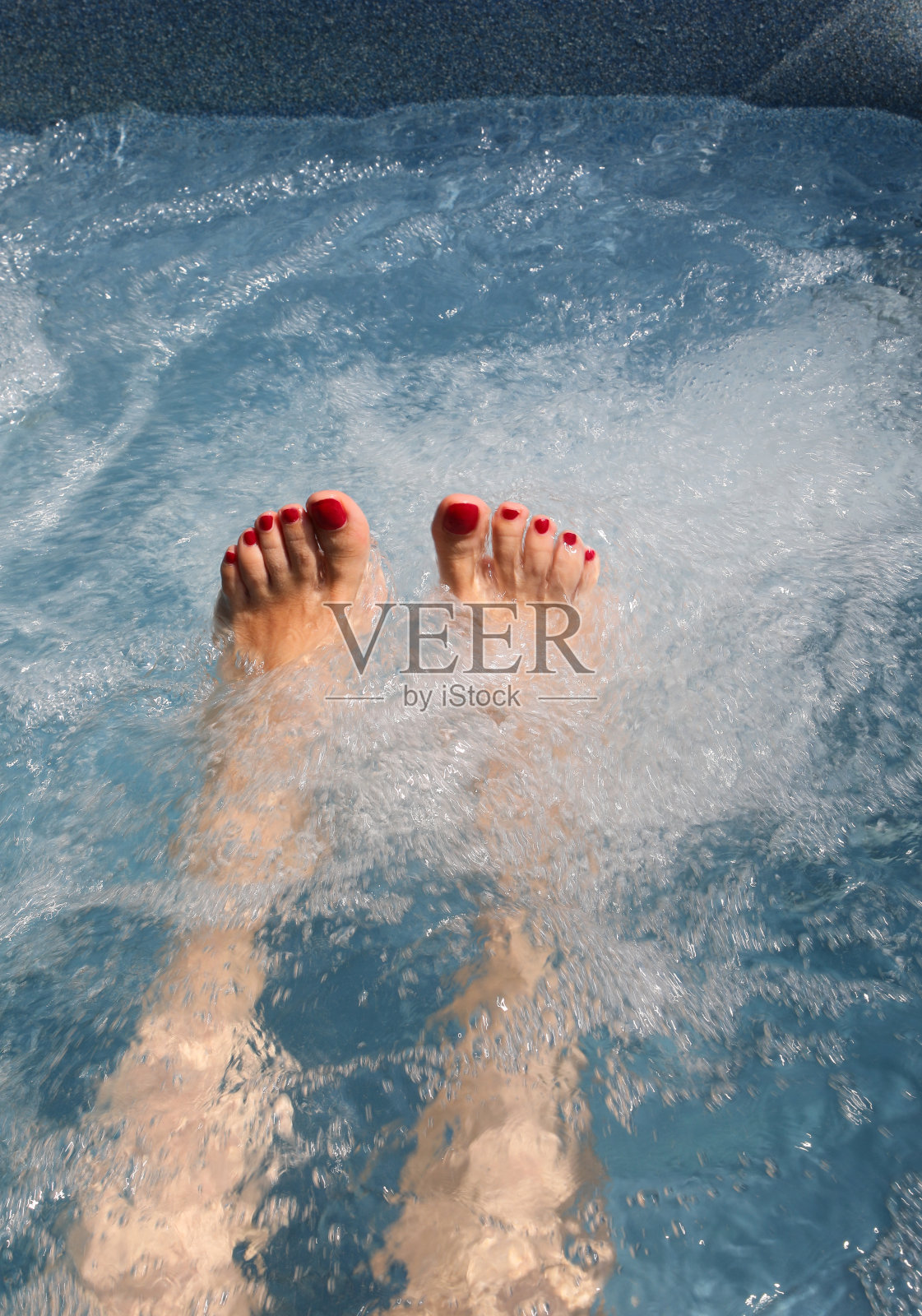 涂着红色指甲油的年轻女子的脚在漩涡浴缸里照片摄影图片