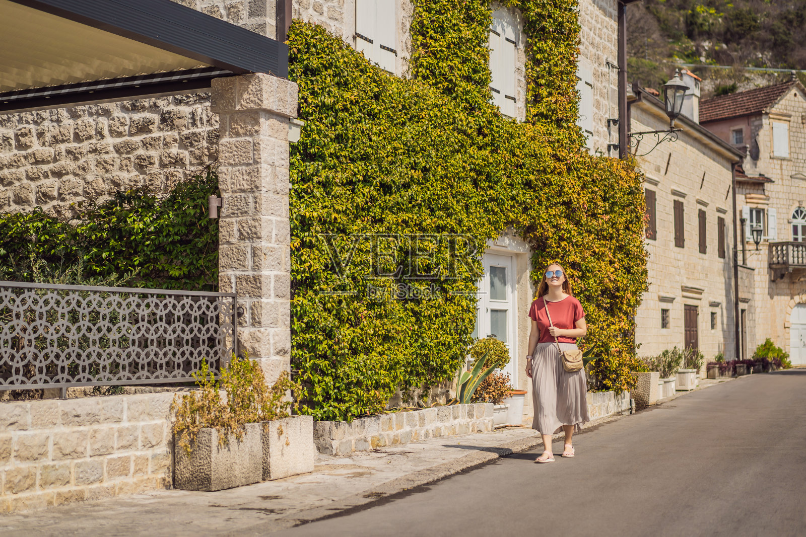 在一个阳光明媚的日子里,女游客在黑山的佩拉斯特老城享受五彩缤纷的街道。黑山旅行的概念。这是著名的科托尔湾的历史小镇佩拉斯特的全景,在一个美丽的阳光明媚的夏日,蓝天白云照片摄影图片