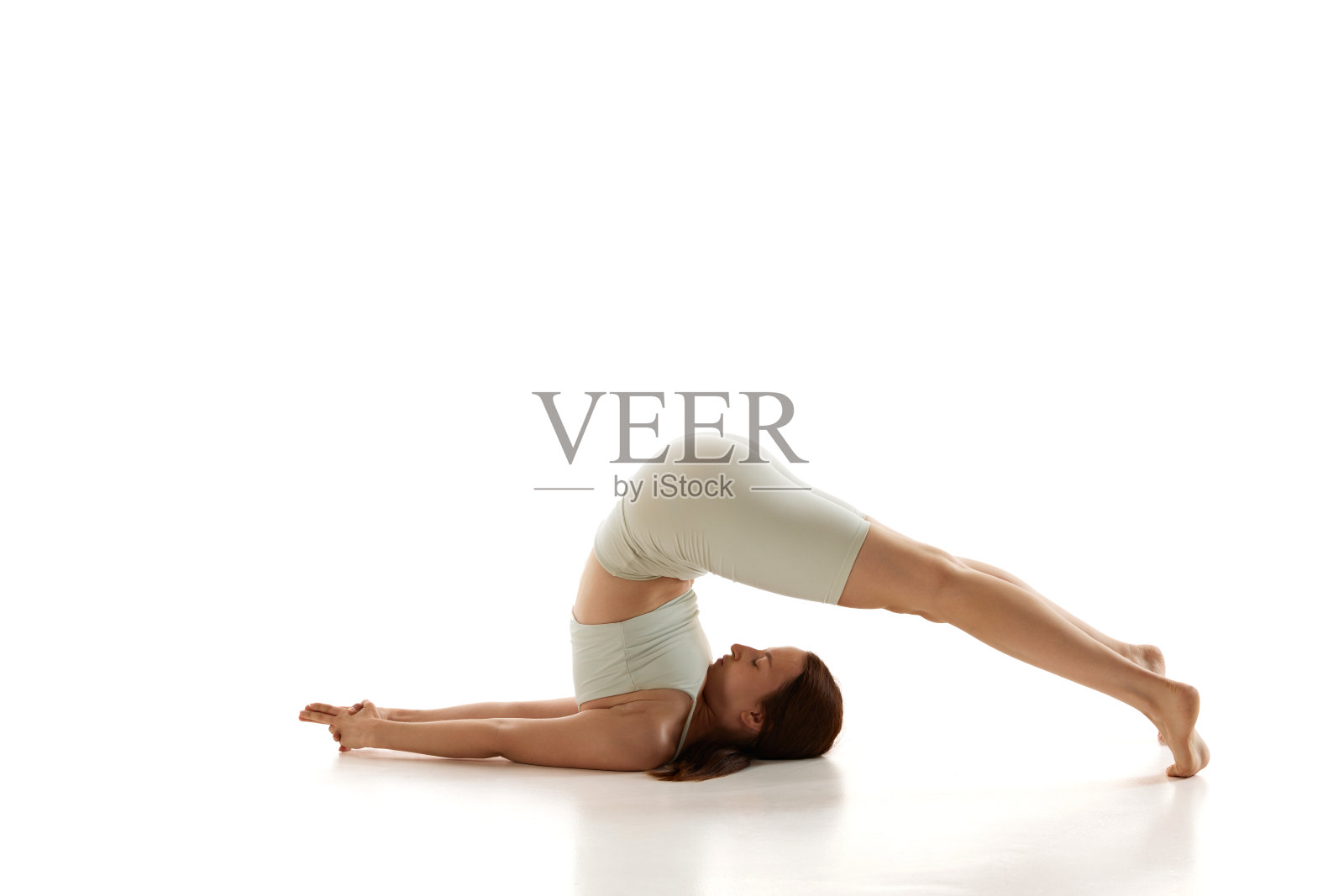 女性练习犁式,专注于脊柱的柔韧性和放松,在白色的工作室背景下训练,以改善身心健康。照片摄影图片