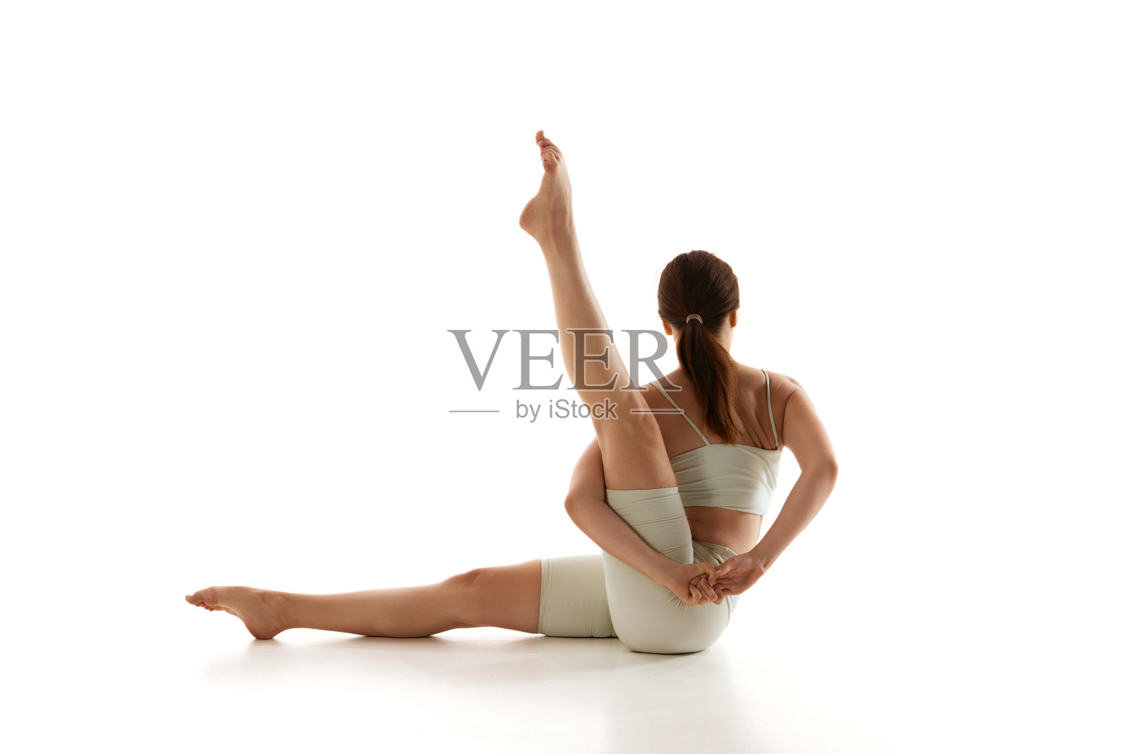 健身妇女练习坐腿伸展与扭转对白色的工作室背景。瑜伽训练和整体身体健康。照片摄影图片