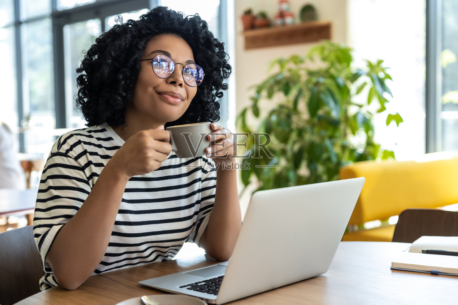 穿着条纹衬衫的女商人一边用笔记本电脑一边喝咖啡照片摄影图片
