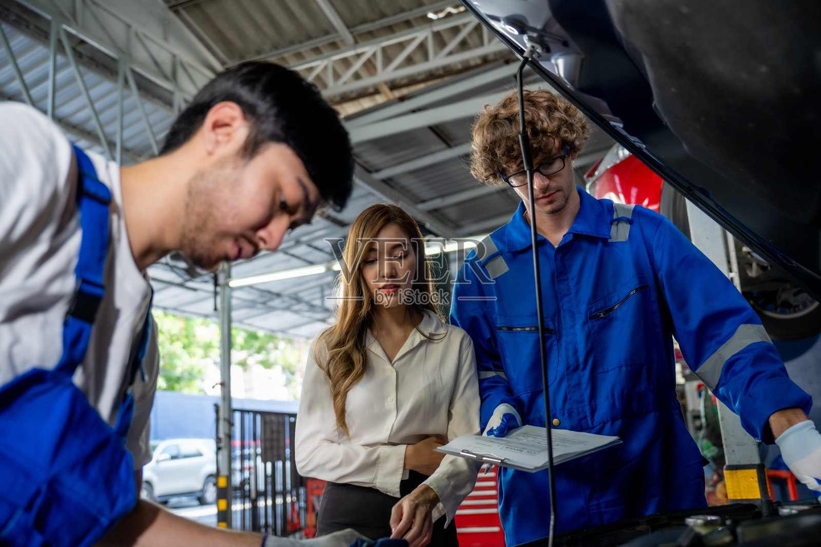 专业汽修师在现代汽车修理厂与客户讨论汽车检验。照片摄影图片