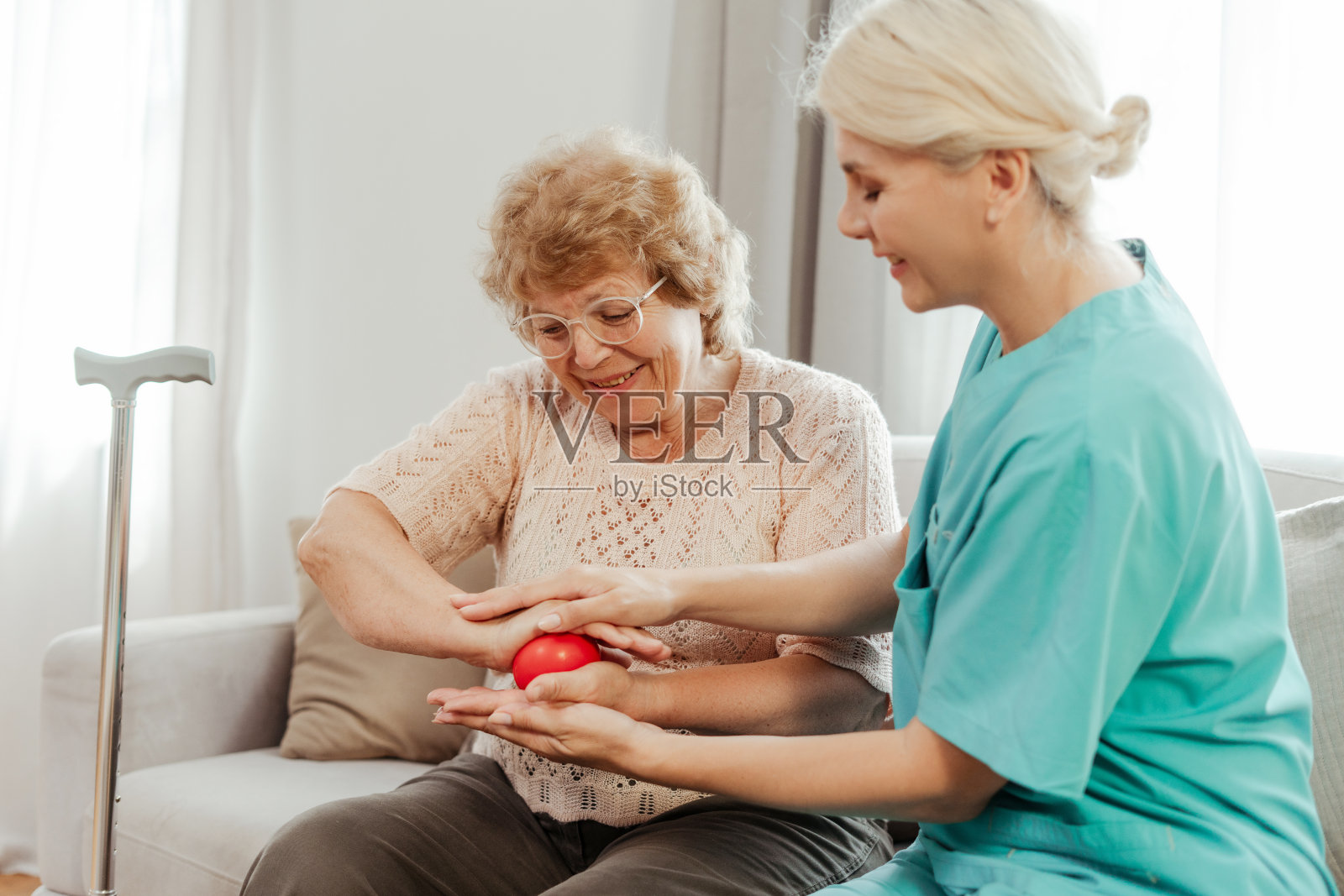 协助老年妇女在家用红球进行康复训练的护士照片摄影图片