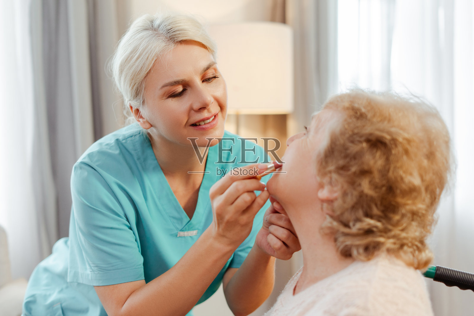 护士在养老院给微笑的老妇人涂口红照片摄影图片