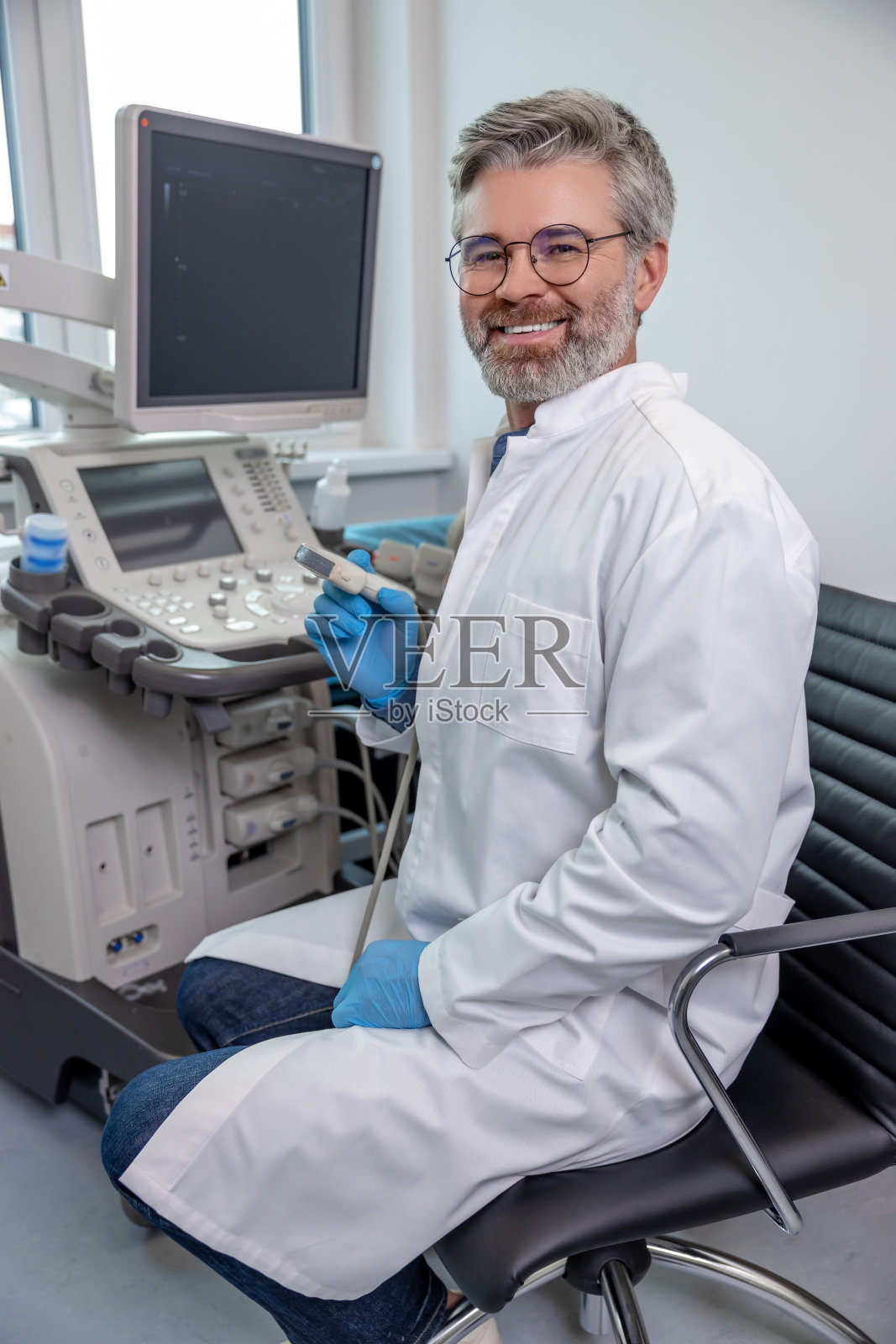 白发苍苍的男性专业人士在超声波检查设备上工作,看起来很自信照片摄影图片