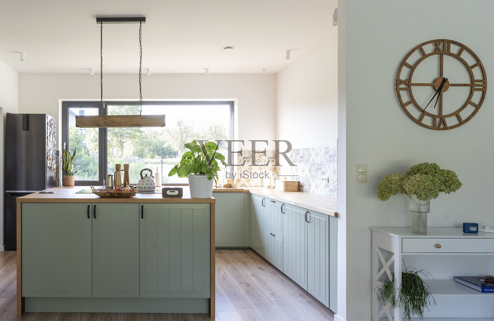 带有挂灯的现代厨房内部,位于带有木制台面和窗户的岛式厨房上方。设计舒适的新公寓。照片摄影图片