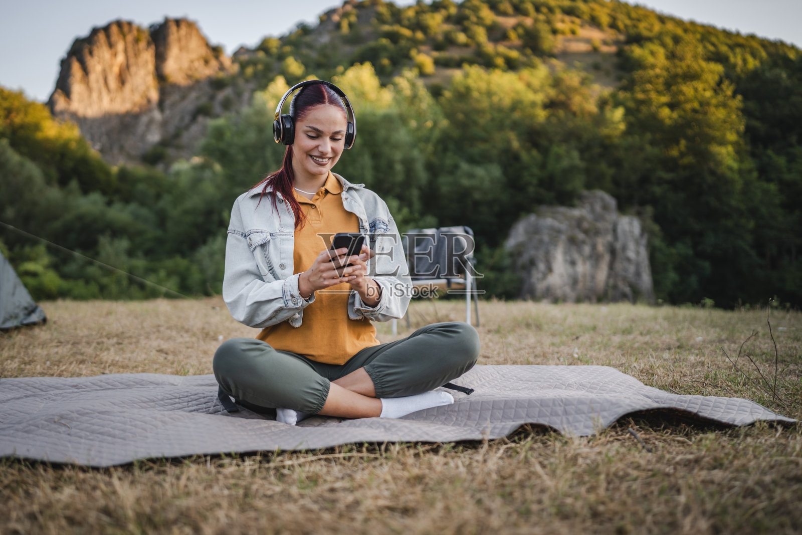 年轻女子戴着耳机听音乐,坐在毯子上照片摄影图片