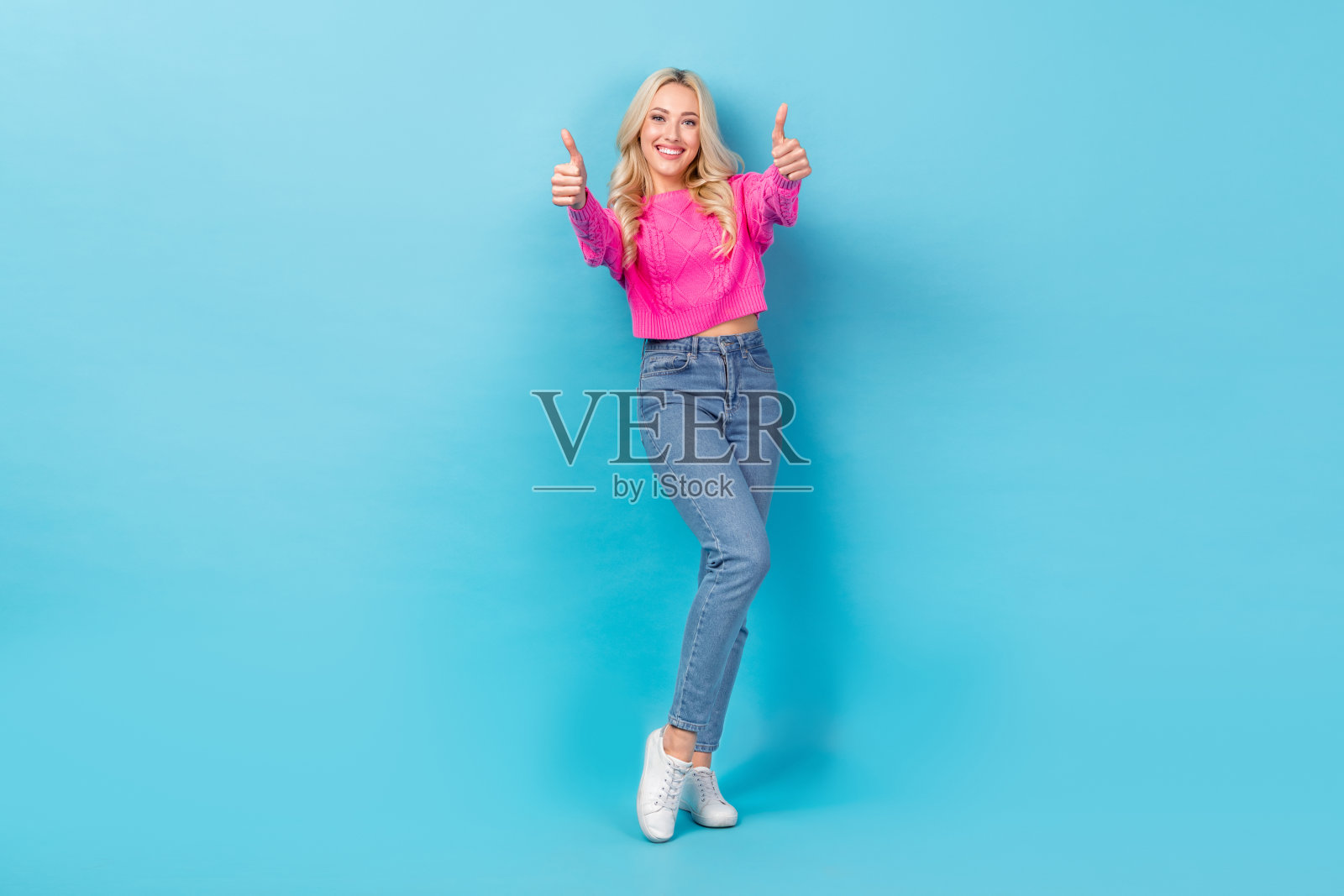 乐观的人的全身照片,卷发,穿着针织毛衣,在蓝色背景上显示大拇指向上赞许照片摄影图片