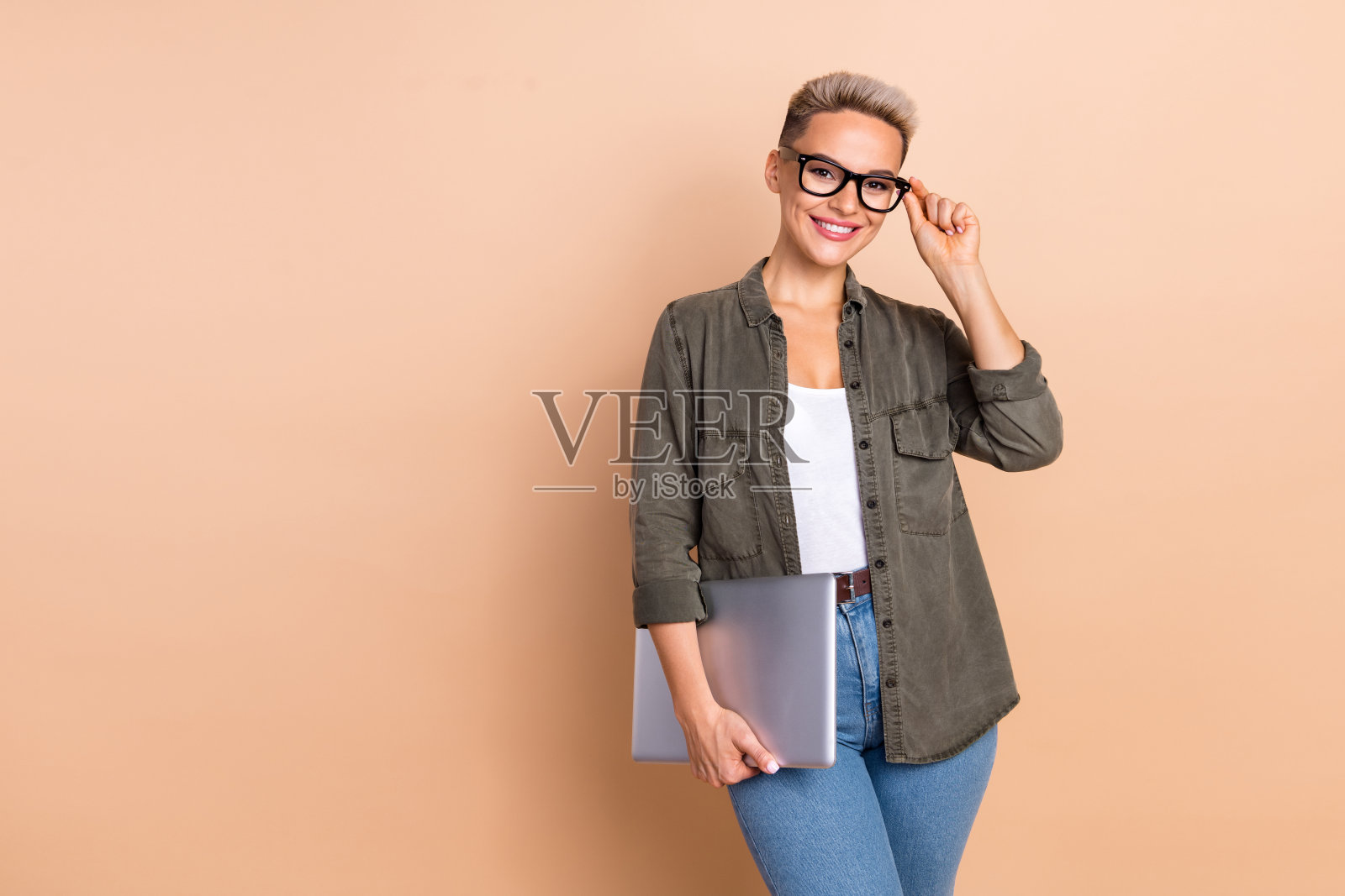 照片中开朗甜美的女士穿着卡其色衬衫,手持苹果三星设备,空空荡荡的米色背景照片摄影图片