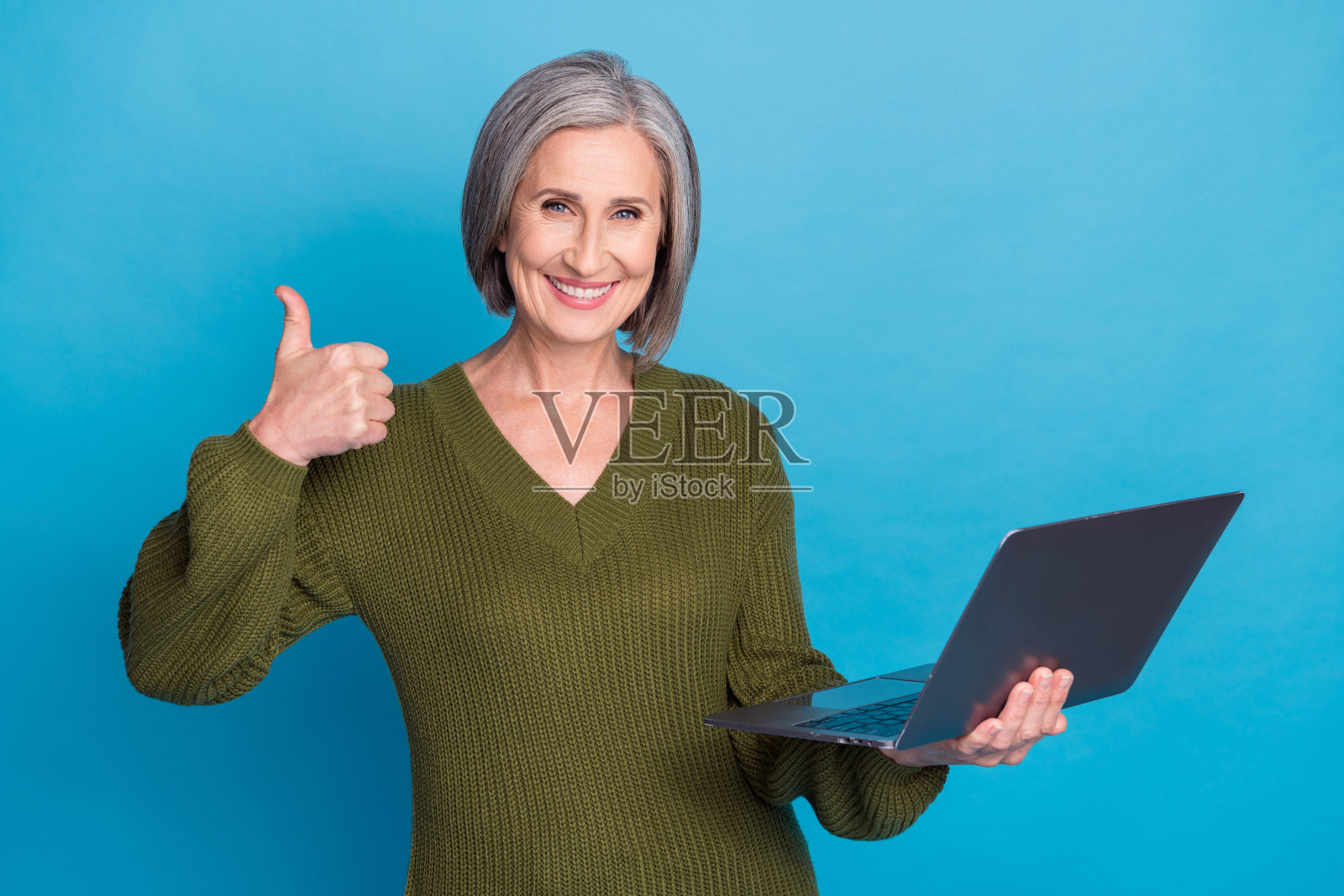 照片友好的人与鲍勃发型穿着针织套头衫拿着笔记本电脑显示拇指向上批准孤立的蓝色背景照片摄影图片