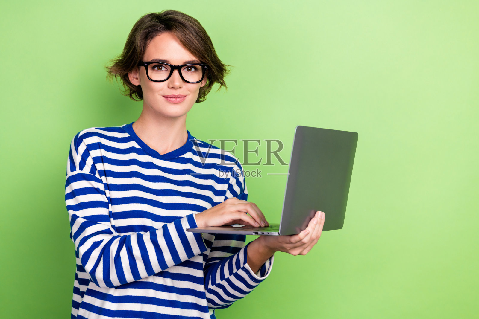 乐观的好心情女人的肖像鲍勃发型穿着条纹运动衫拿着笔记本电脑打字电子邮件孤立的绿色背景照片摄影图片