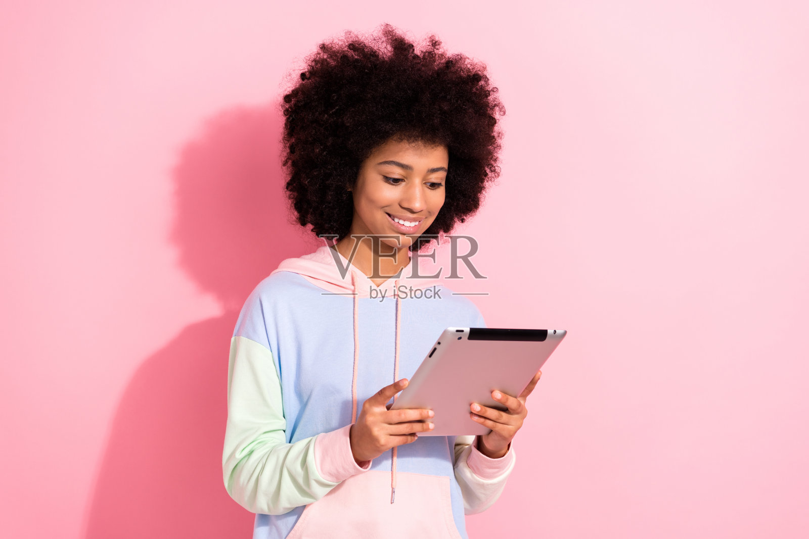 开朗的小学生的牙齿微笑的照片拿着使用上网本在线课程孤立在粉红色的背景照片摄影图片