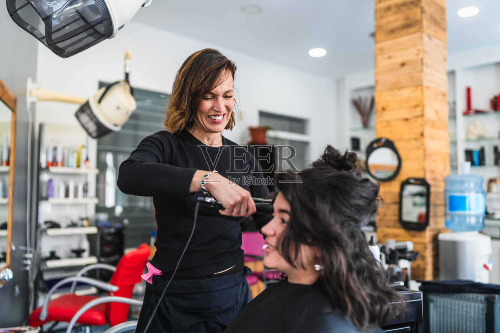 在明亮的沙龙里,微笑的理发师正在给顾客拉直头发照片摄影图片