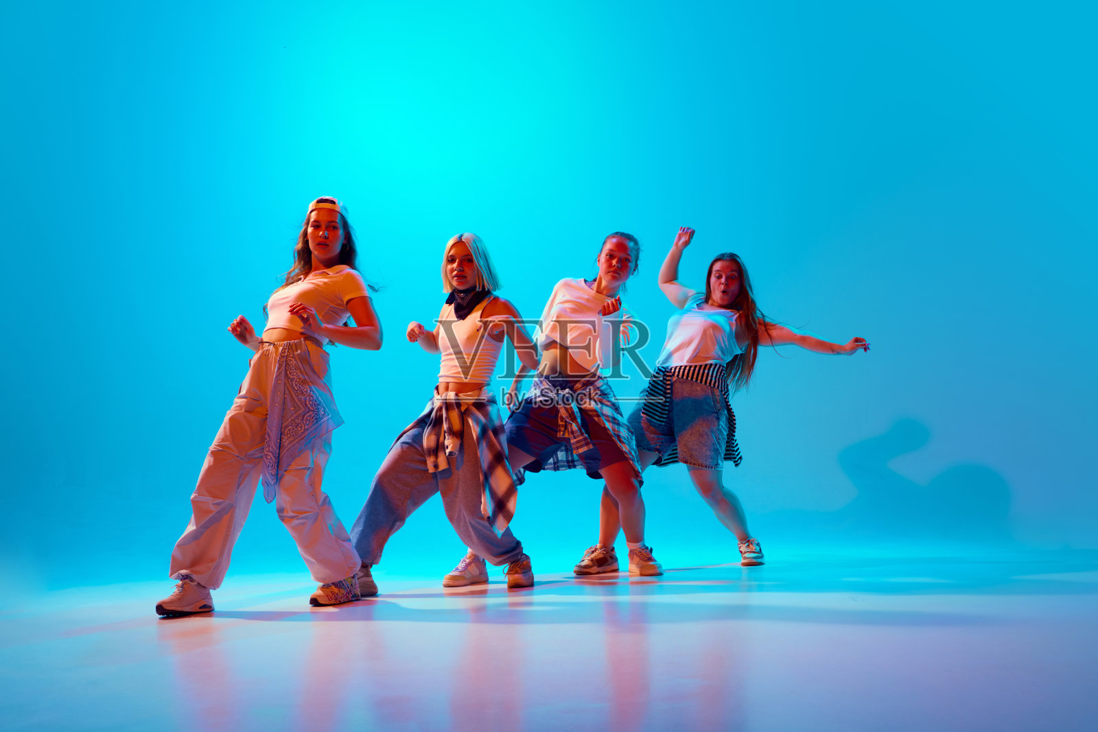 活泼的四名舞者穿着复古休闲装,在蓝色灯光下大胆地摆姿势,捕捉他们独特的风格和活力。照片摄影图片
