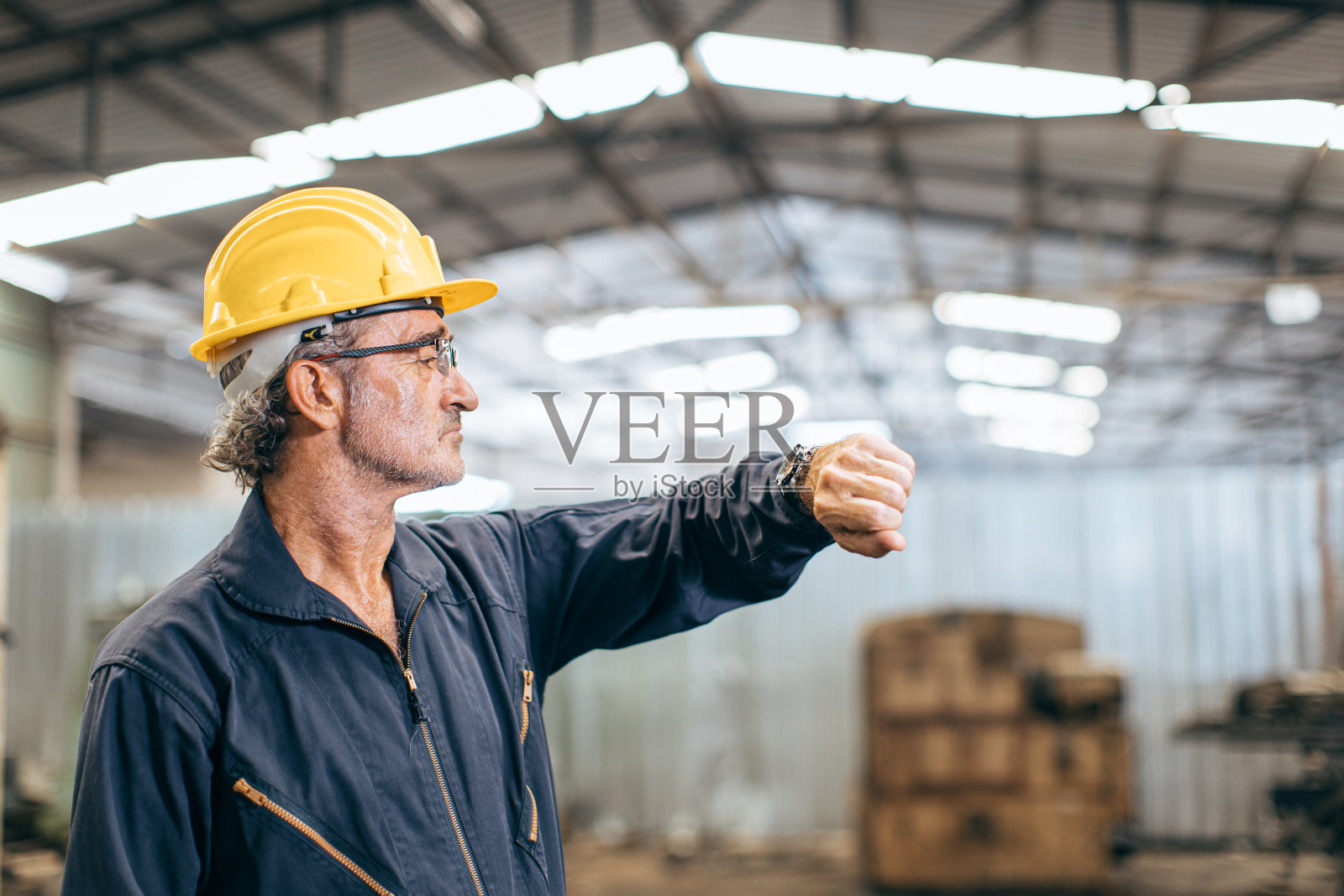 高级工人看着手表上的时钟等待工作时间午餐刹车。照片摄影图片