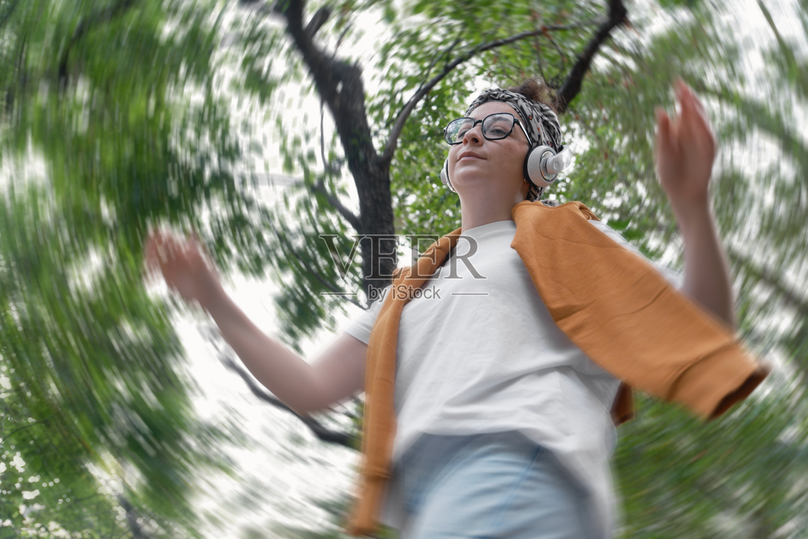 一个戴着耳机,穿着黄色夹克的女人站在森林里照片摄影图片