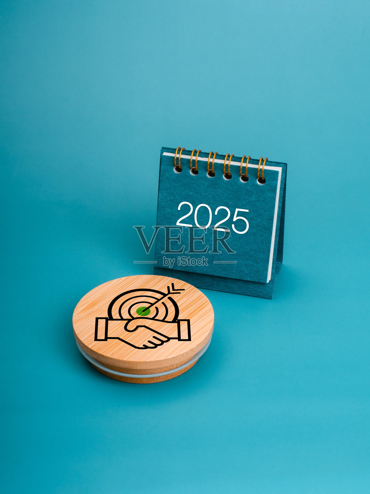 商务合作,环保理念,祝2025年新年快乐。小2025台历和握手目标图标在圆木立方体块垂直蓝色背景,最小的风格。照片摄影图片