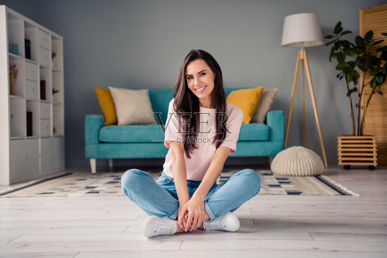 照片中闪亮甜美的年轻女孩穿着粉红色的t恤,微笑着坐在地板上,双腿交叉,在家里的房间里休息放松照片摄影图片