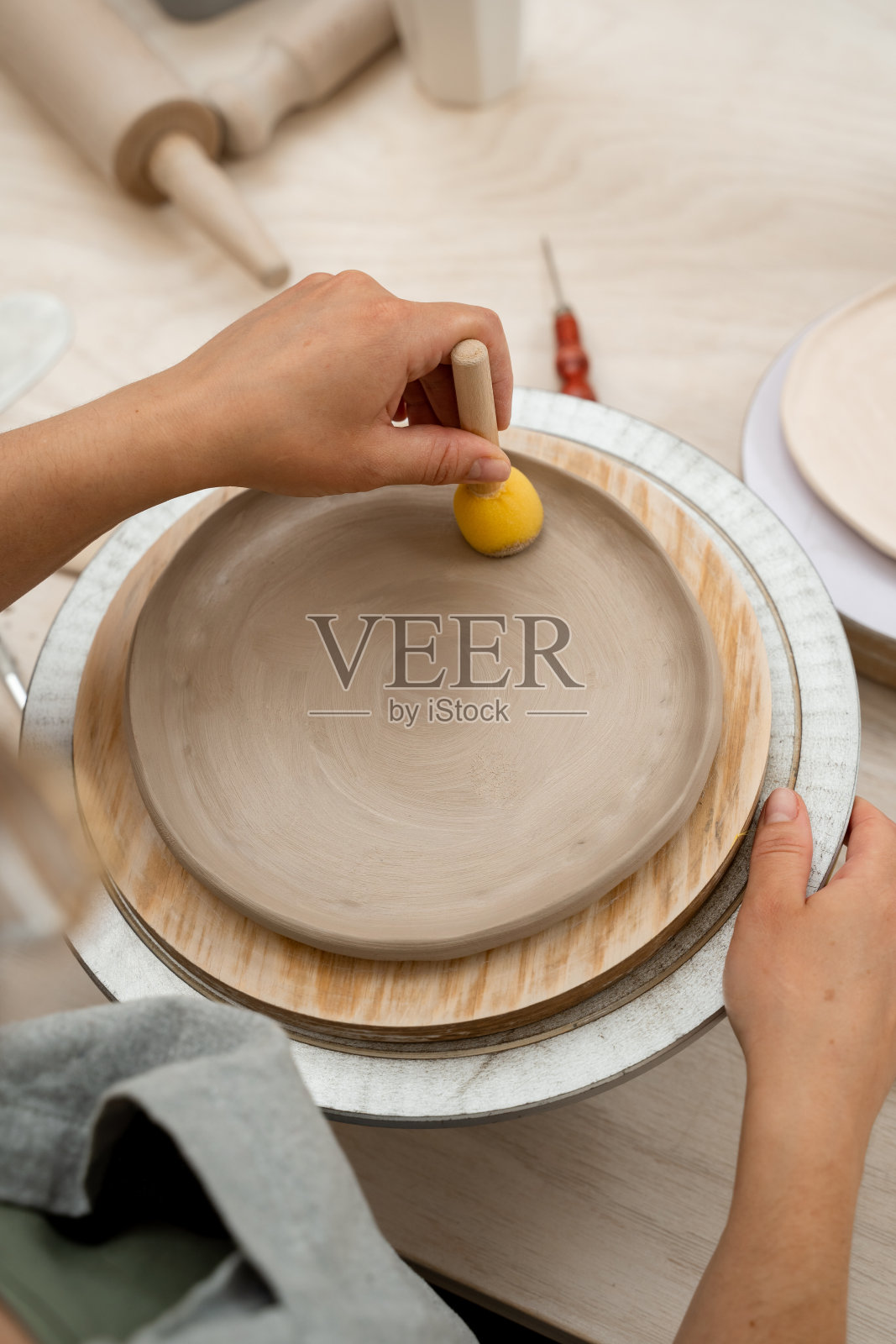 女孩正在用一根棍子上的海绵塑造陶器的形状,并从粘土中吸收多余的水分。在陶器作坊里用木柄海绵擦亮粘土制品的表面。照片摄影图片