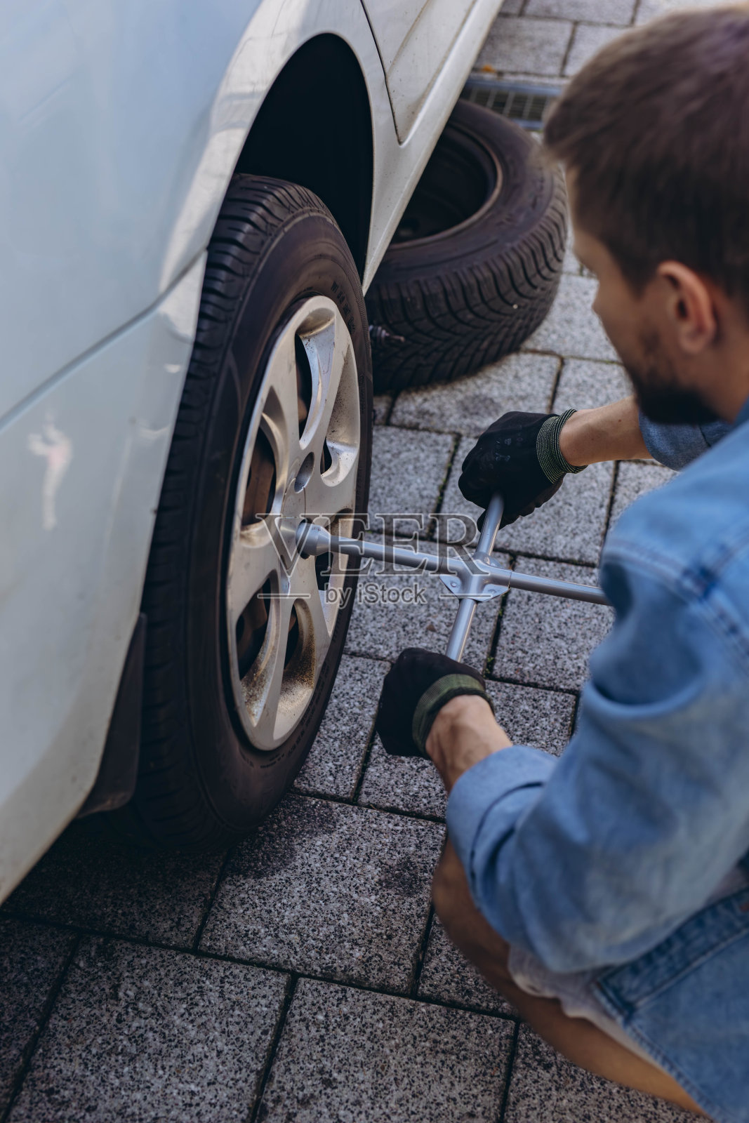 年轻人在更换新轮胎的过程中,用扳手拧开车轮上的凸耳螺母,同时在路上换瘪胎。照片摄影图片