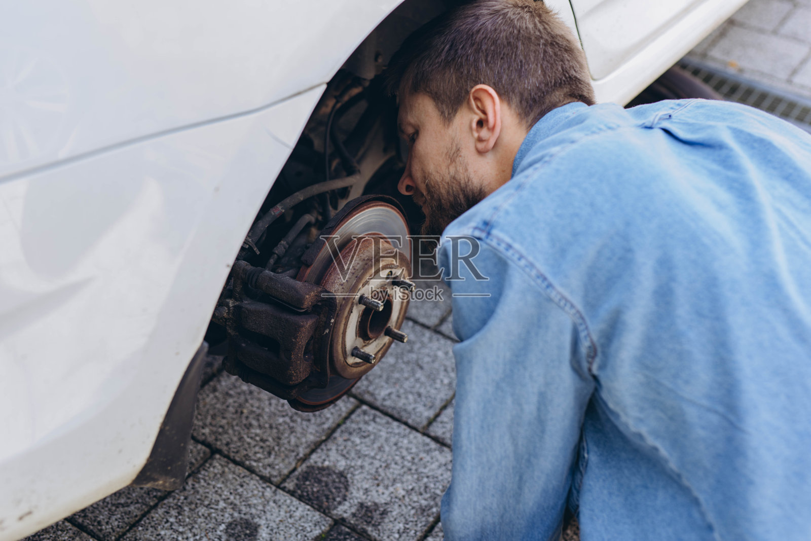 年轻人在更换新轮胎的过程中,用扳手拧开车轮上的凸耳螺母,同时在路上换瘪胎。照片摄影图片
