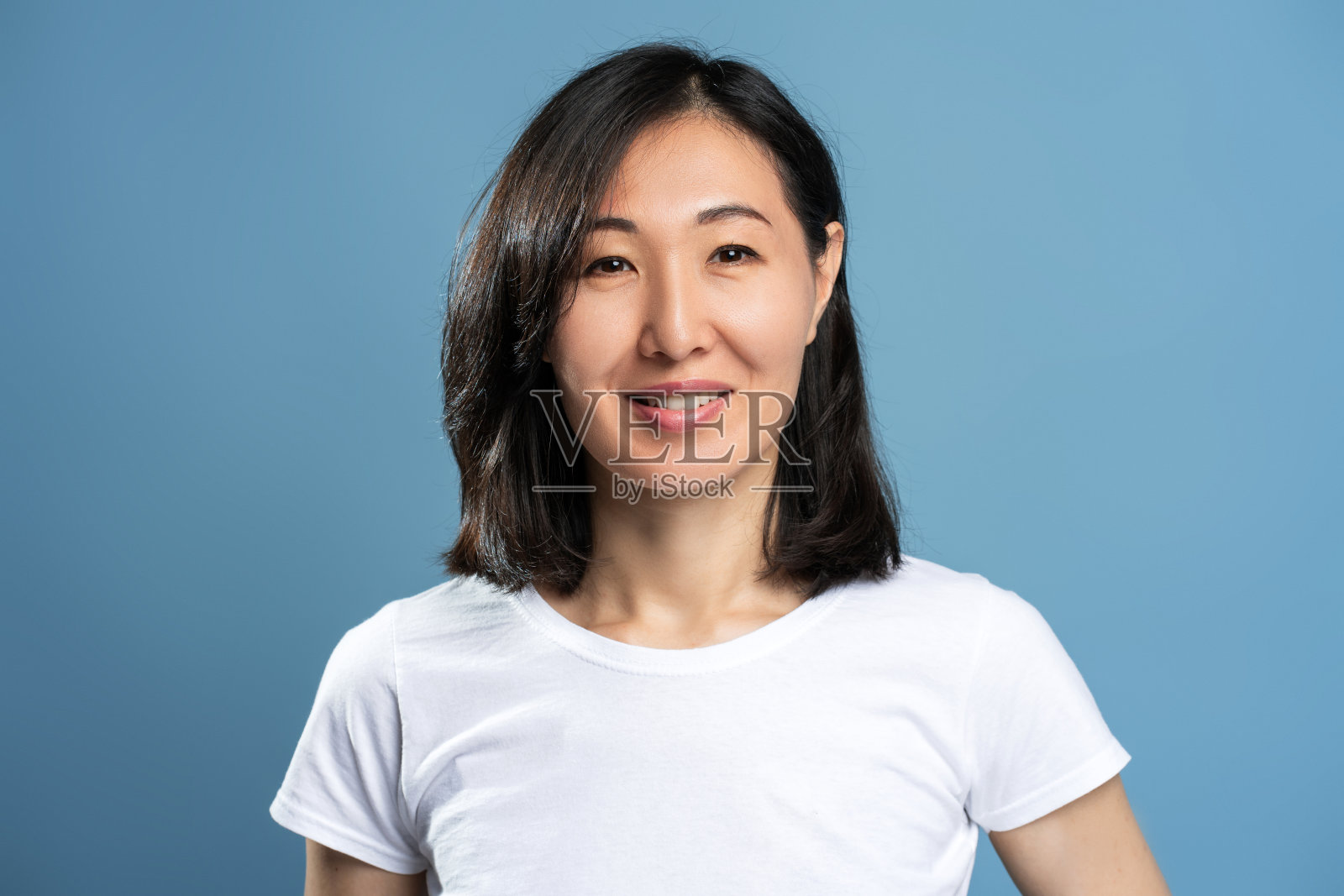 穿着白色t恤的亚洲女人微笑着站在蓝色背景上看镜头照片摄影图片