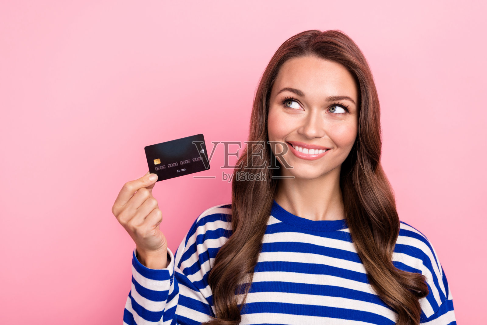 可爱可爱的女孩的肖像卷发条纹衣服持有信用卡看起来空空间销售孤立在粉红色的背景照片摄影图片
