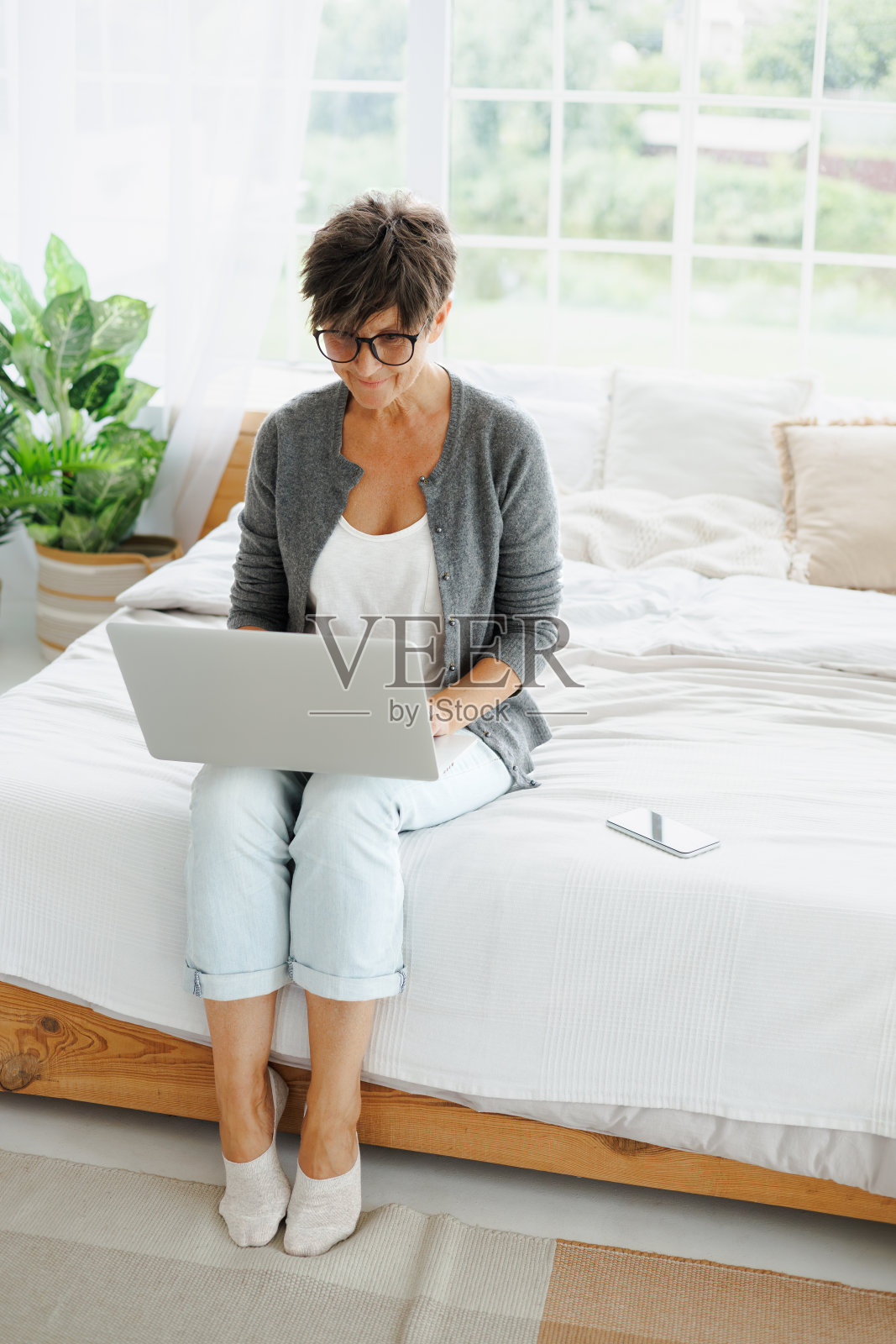 戴眼镜的成熟的女人在家里的床上使用笔记本电脑照片摄影图片
