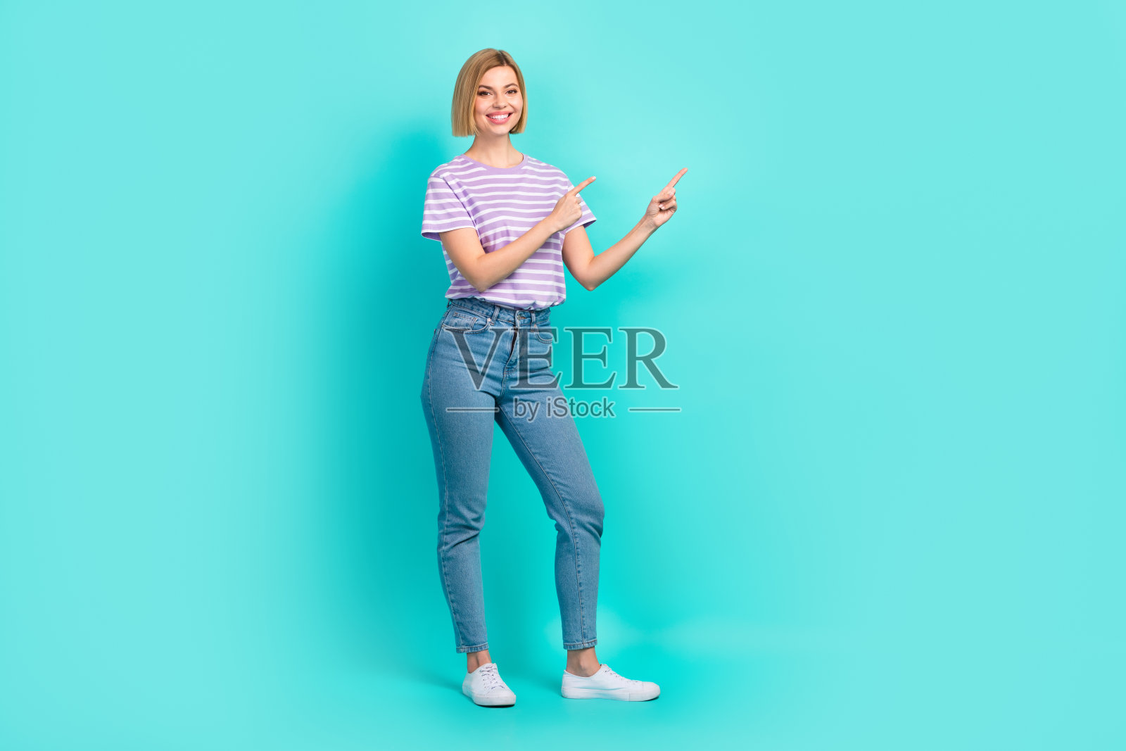 年轻模特穿着时尚服装的全身照片,手指指向空旷的空间,在海蓝宝石的背景上打开品牌商店照片摄影图片