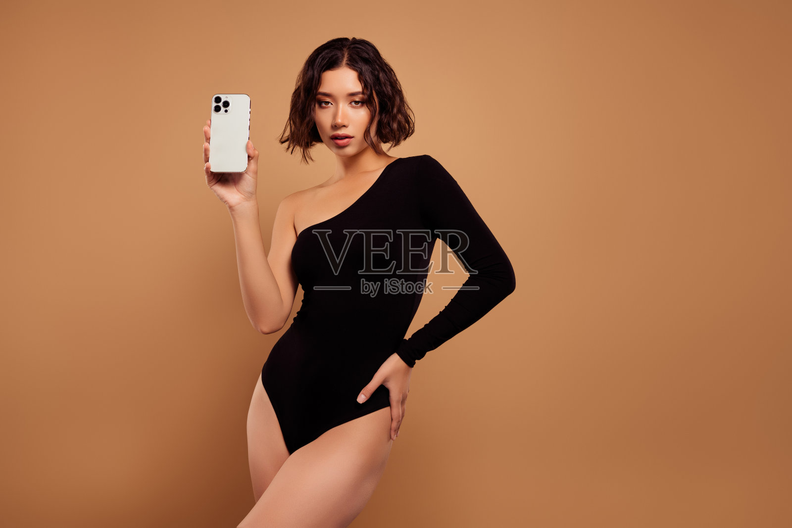 照片上的梦幻妖娆的女士穿着脱肩黑色紧身衣,展示装置空旷的空间孤立的米色背景照片摄影图片