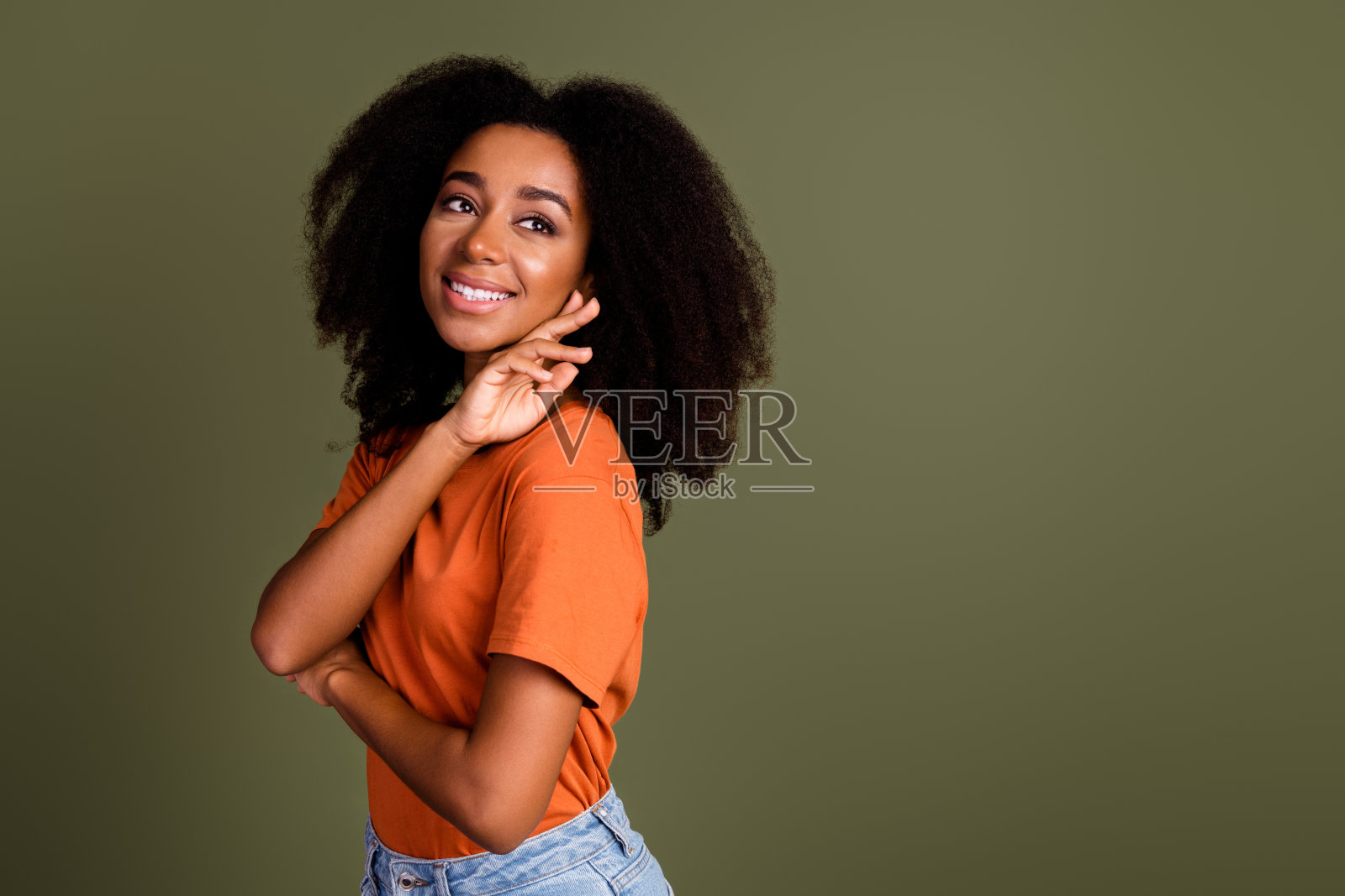 照片中迷人积极的女人穿着橙色t恤微笑着看着空旷孤立的卡其色背景照片摄影图片