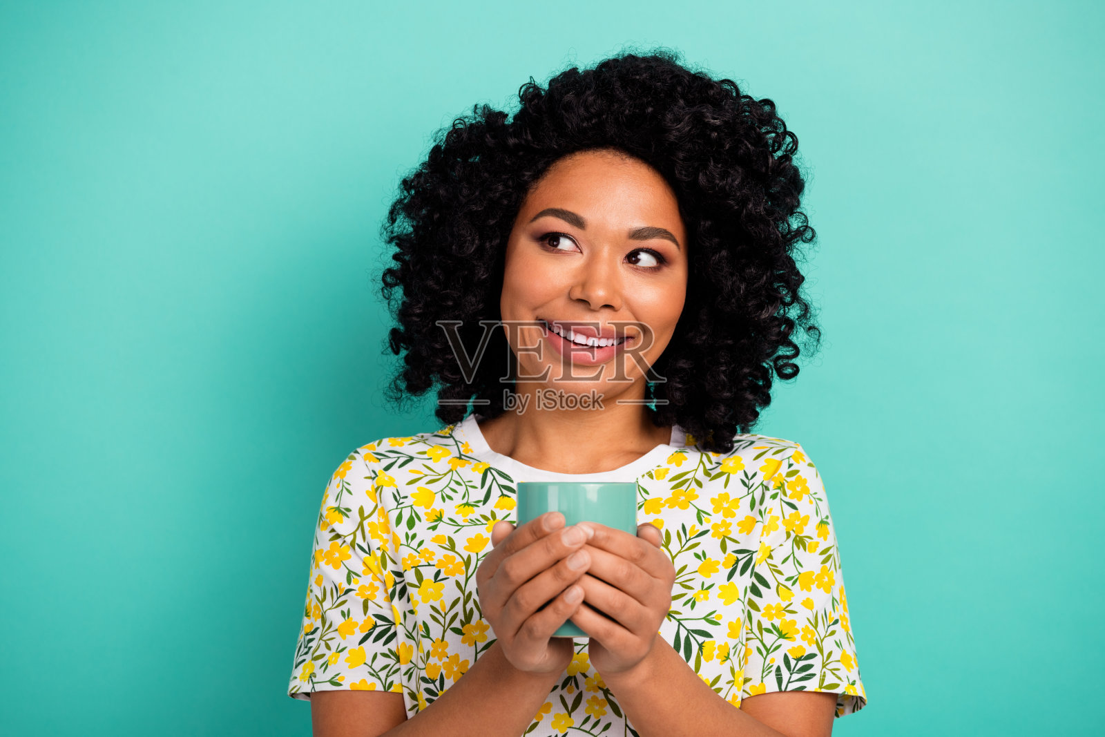 照片中开朗漂亮的女士穿着黄色t恤喝茶,看起来空旷孤立的蓝绿色背景照片摄影图片