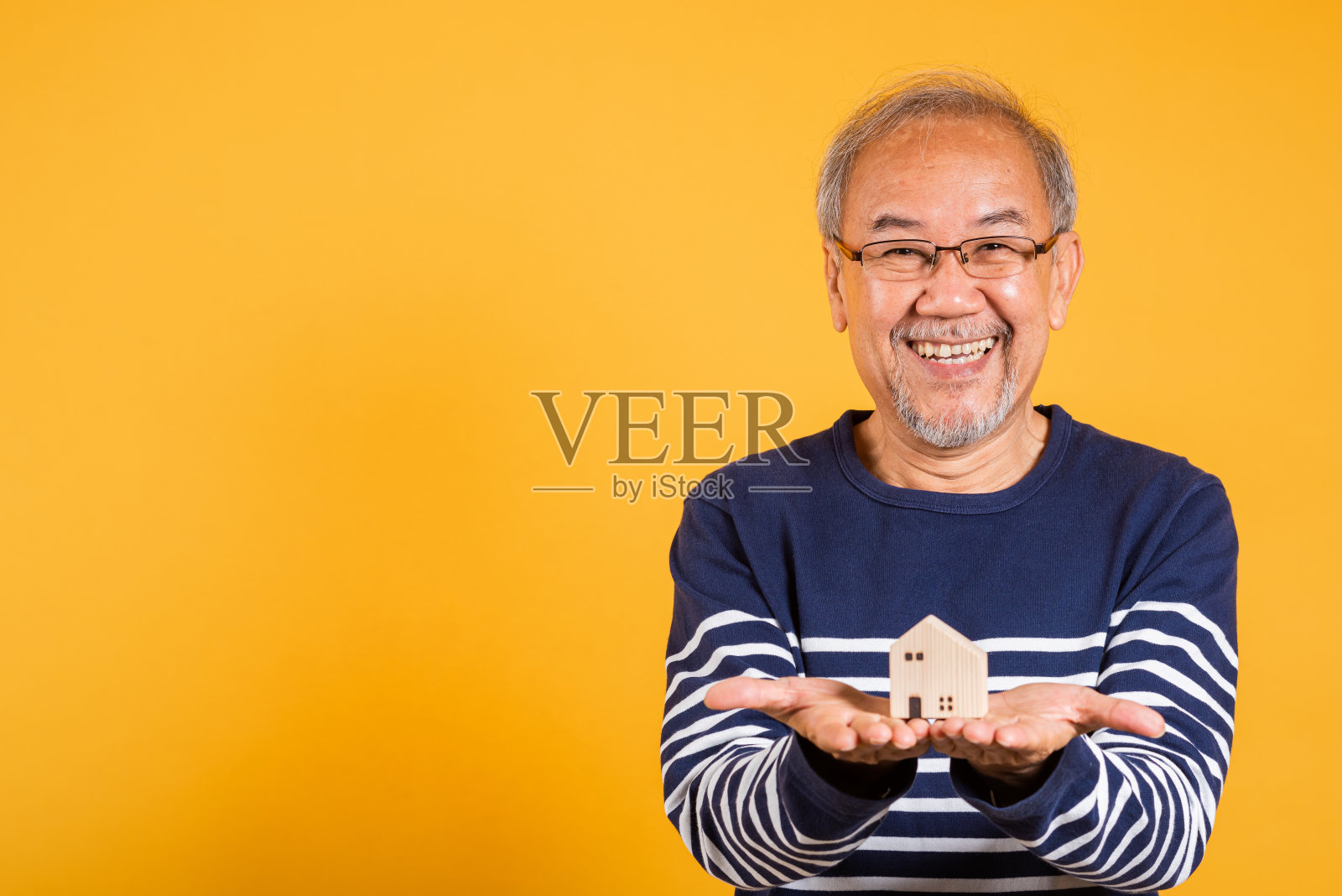 肖像亚洲面带微笑的老人带着眼镜拿着小房子模特工作室拍摄孤立的黄色背景,快乐的老人白发老人照片摄影图片