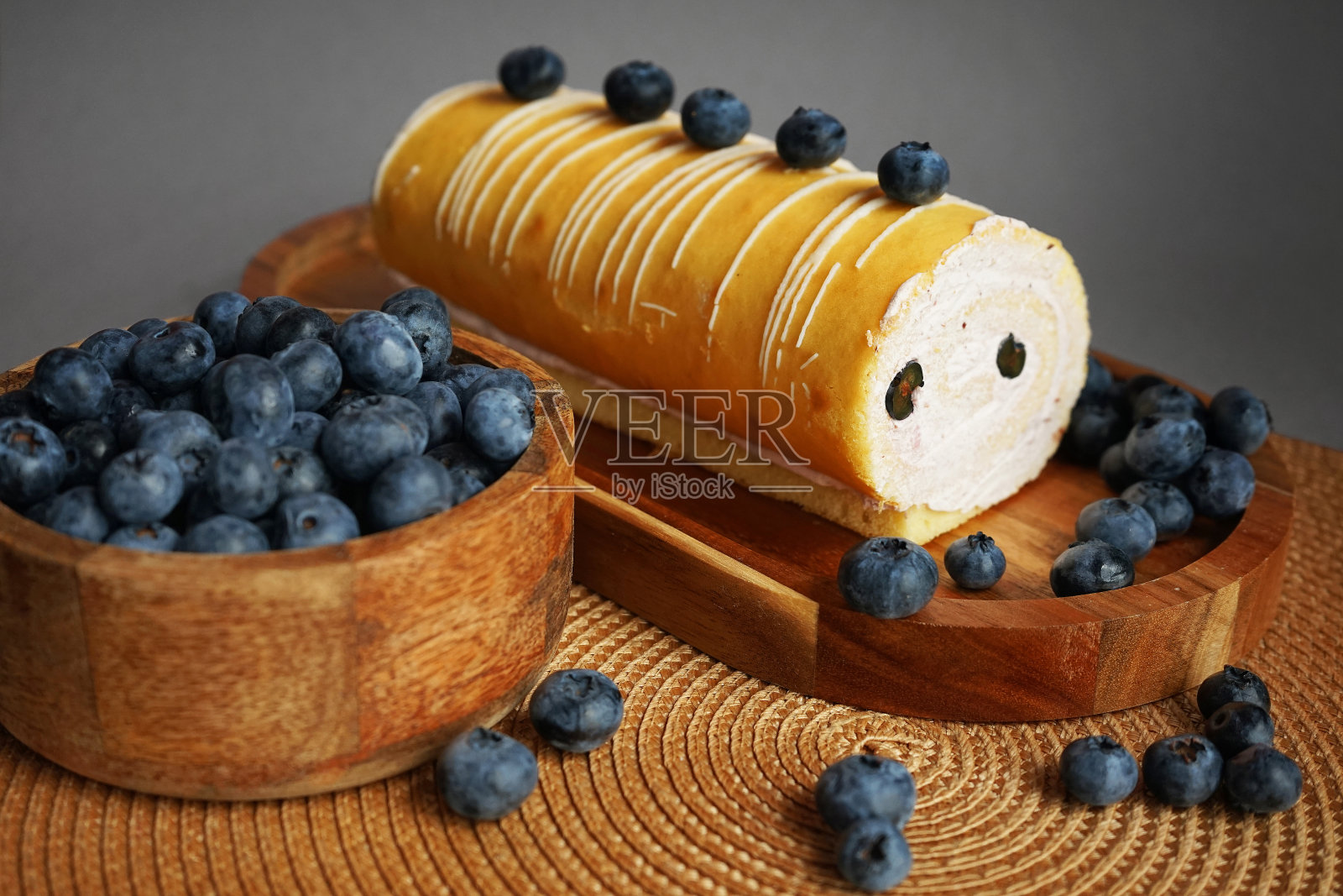 木质托盘上放着奶油和蓝莓的海绵卷,旁边是一碗米色餐巾上的新鲜浆果照片摄影图片