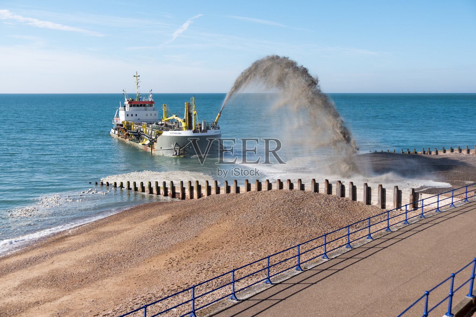 在伊斯特本,挖泥船向海滩上喷洒碎石。照片摄影图片