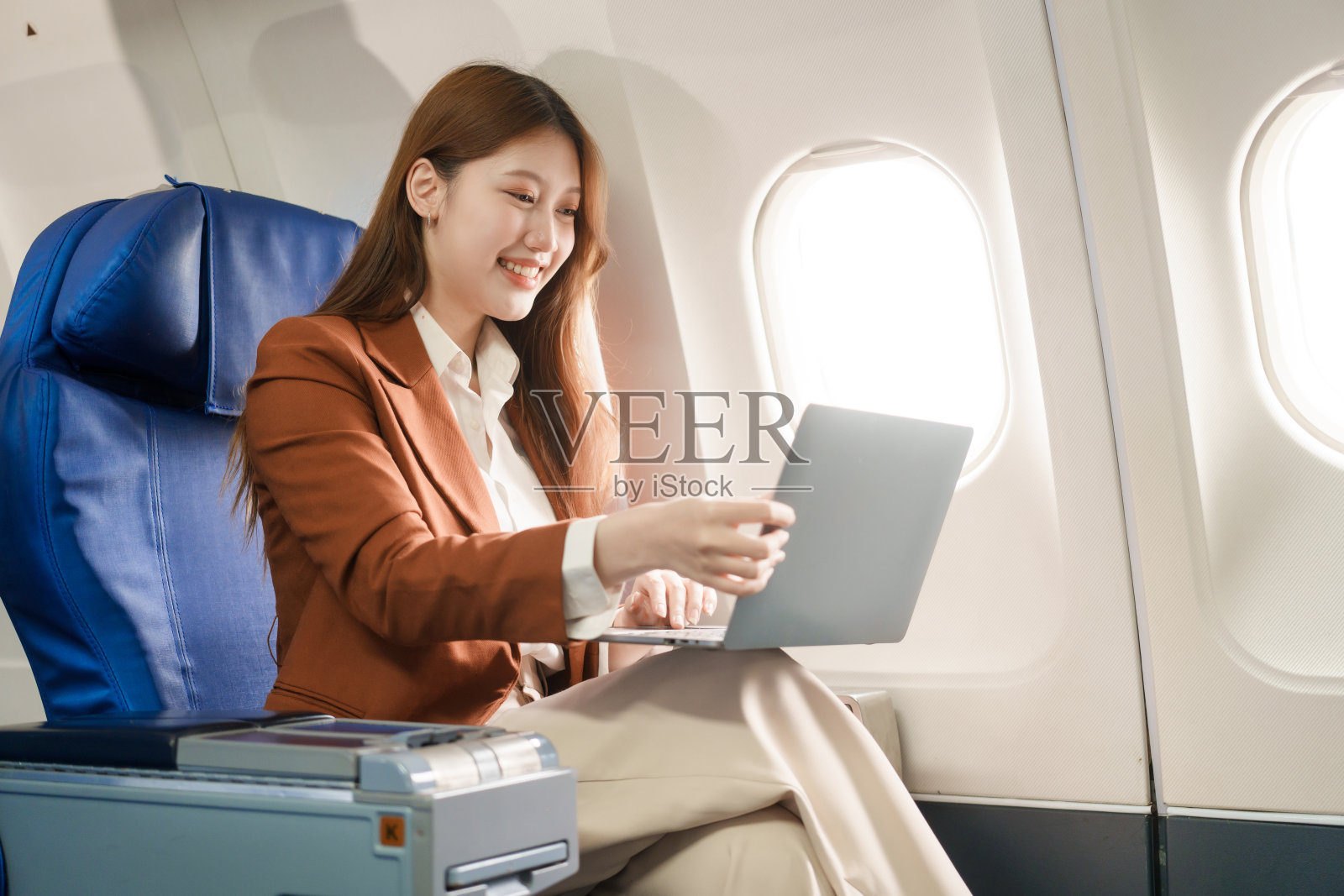 一位女商人乘飞机出国旅行,在飞行过程中,她一边在窗外拍照,一边使用电脑。她在享受旅行的同时平衡了工作和休闲。照片摄影图片