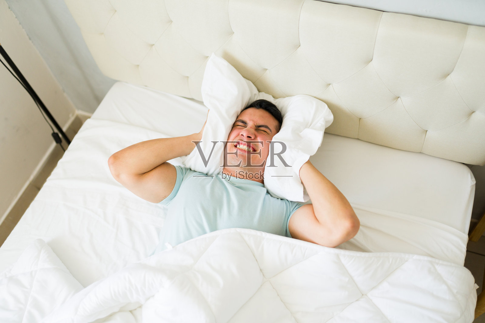 一名压力大、心烦意乱的男子躺在床上,用枕头挡住邻居的噪音照片摄影图片