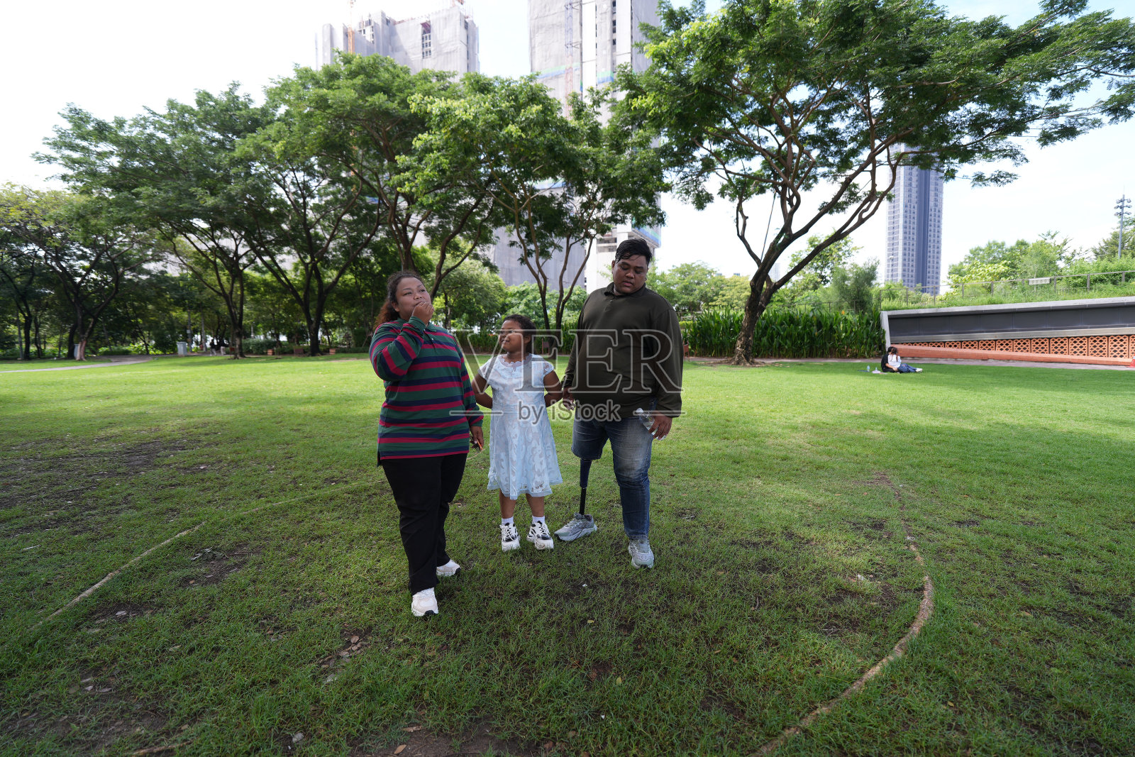 一个又大又胖的亚洲家庭,爸爸、妈妈、女儿在公园里野餐,他们坐着吃零食。他们坐着做作业,互相送花。他们很开心。照片摄影图片