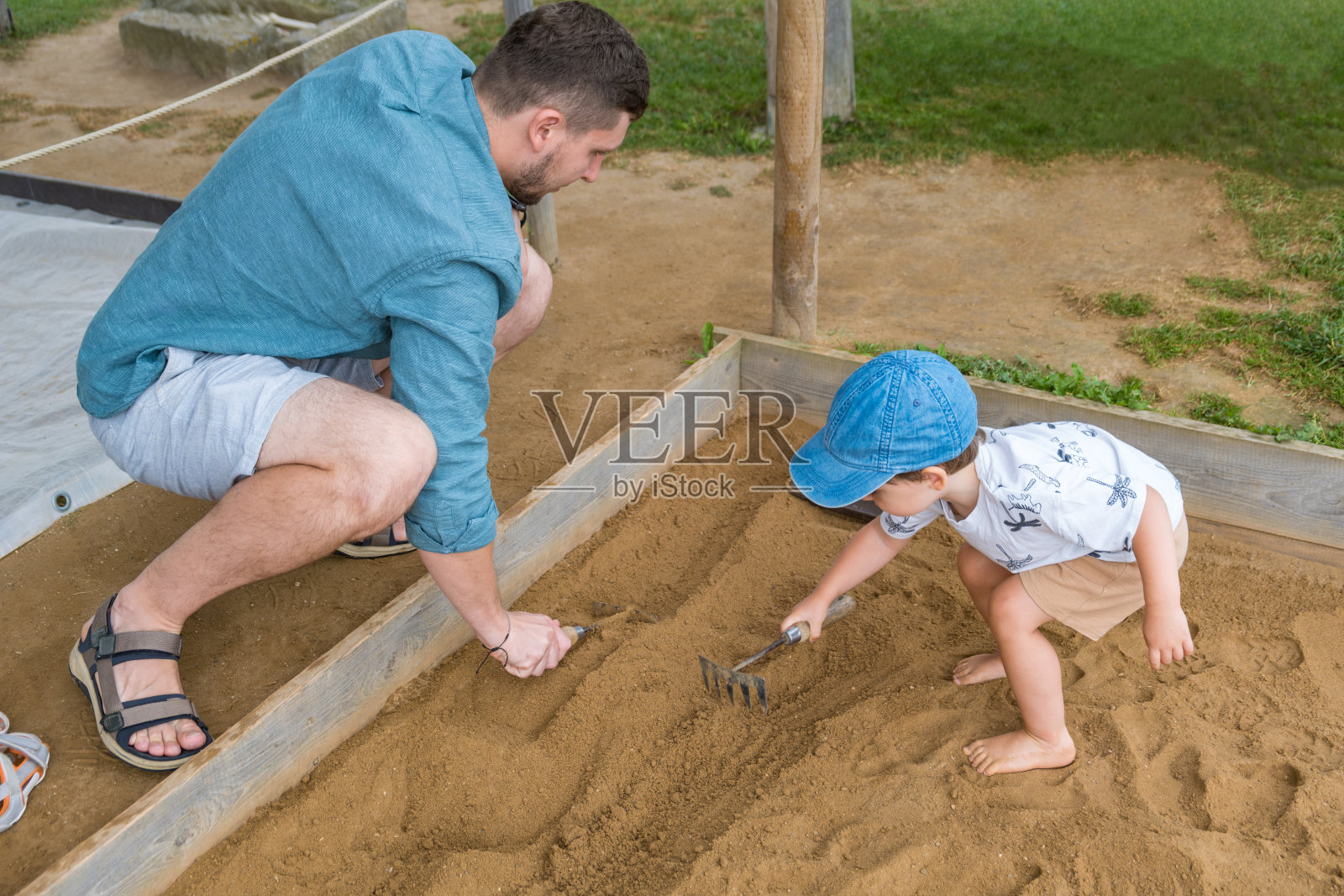 爸爸和儿子在考古公园的沙箱里用耙子挖掘照片摄影图片