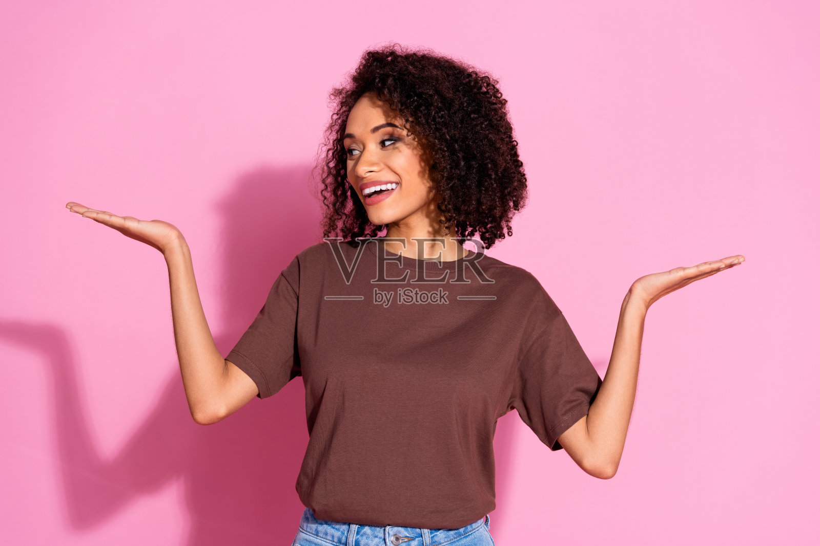 漂亮的年轻女士的肖像手持空的空间尺度穿着棕色t恤孤立在粉红色的背景照片摄影图片