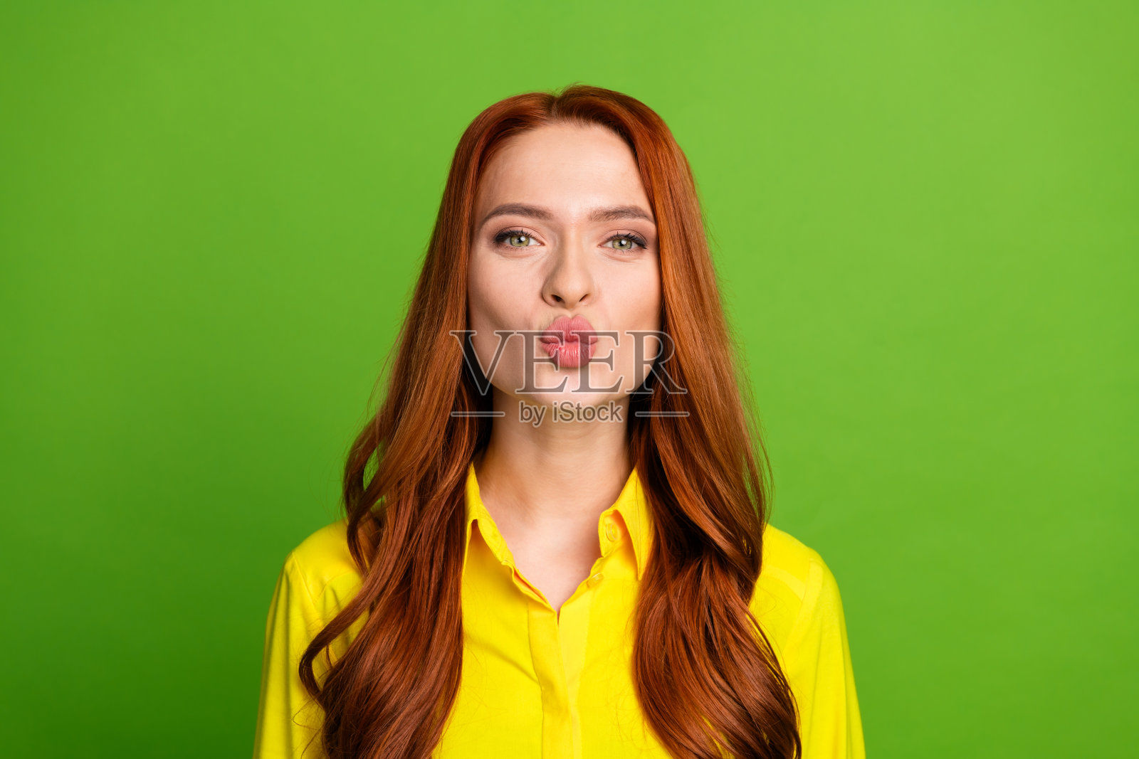 漂亮的年轻女孩亲吻噘起的嘴唇,穿着时髦的黄色衣服,孤立在绿色的背景照片摄影图片