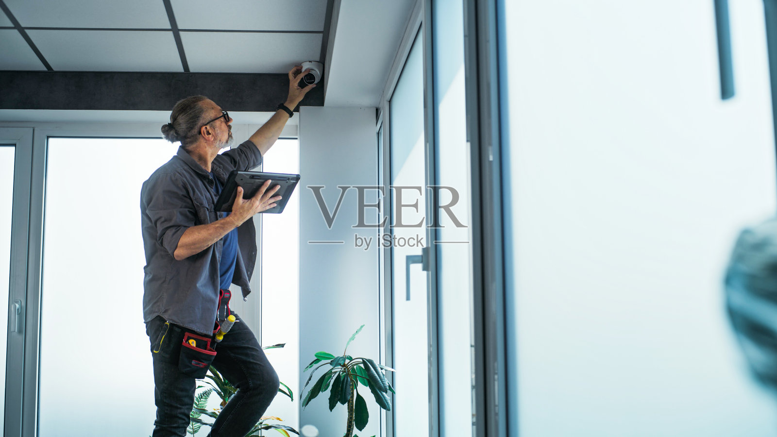 男技术人员站在梯子上,用平板电脑在办公室安装闭路电视摄像机照片摄影图片