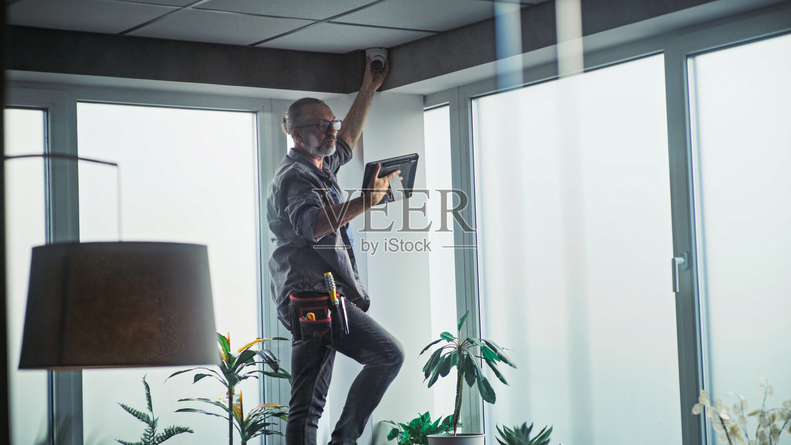 男技术人员站在梯子上,用平板电脑在办公室安装闭路电视摄像机照片摄影图片