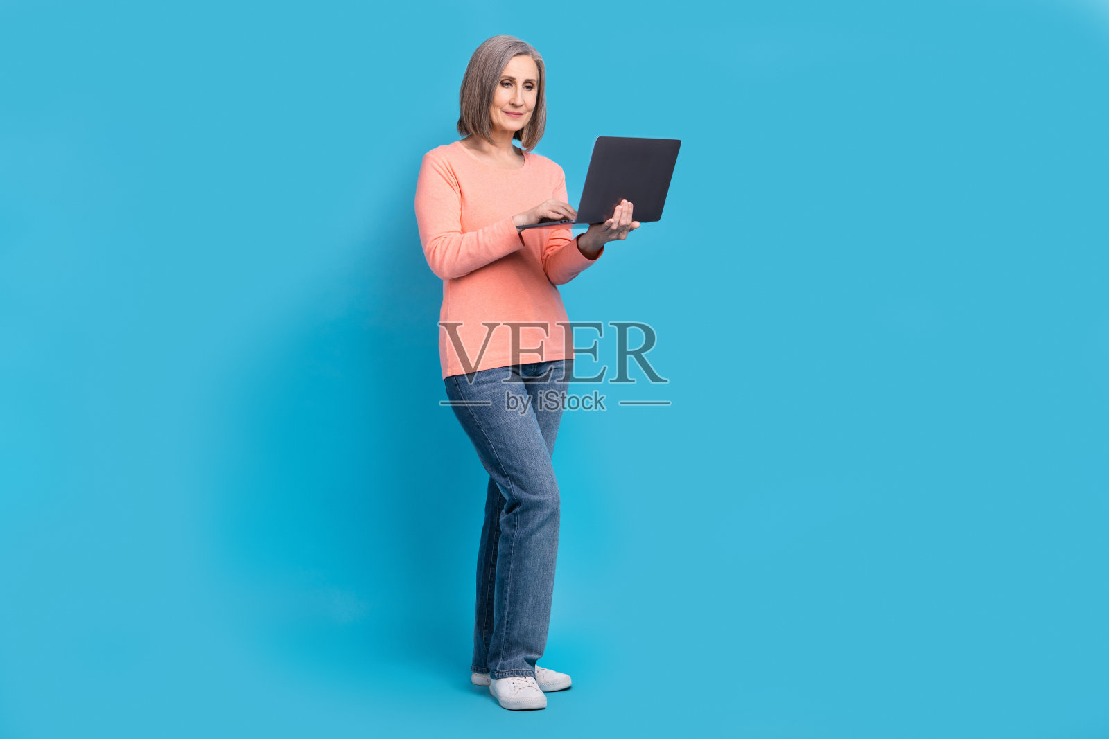 全身干部自信的自由职业者退休妇女持有笔记本电脑互联网编码程序员网页设计师孤立的蓝色背景照片摄影图片