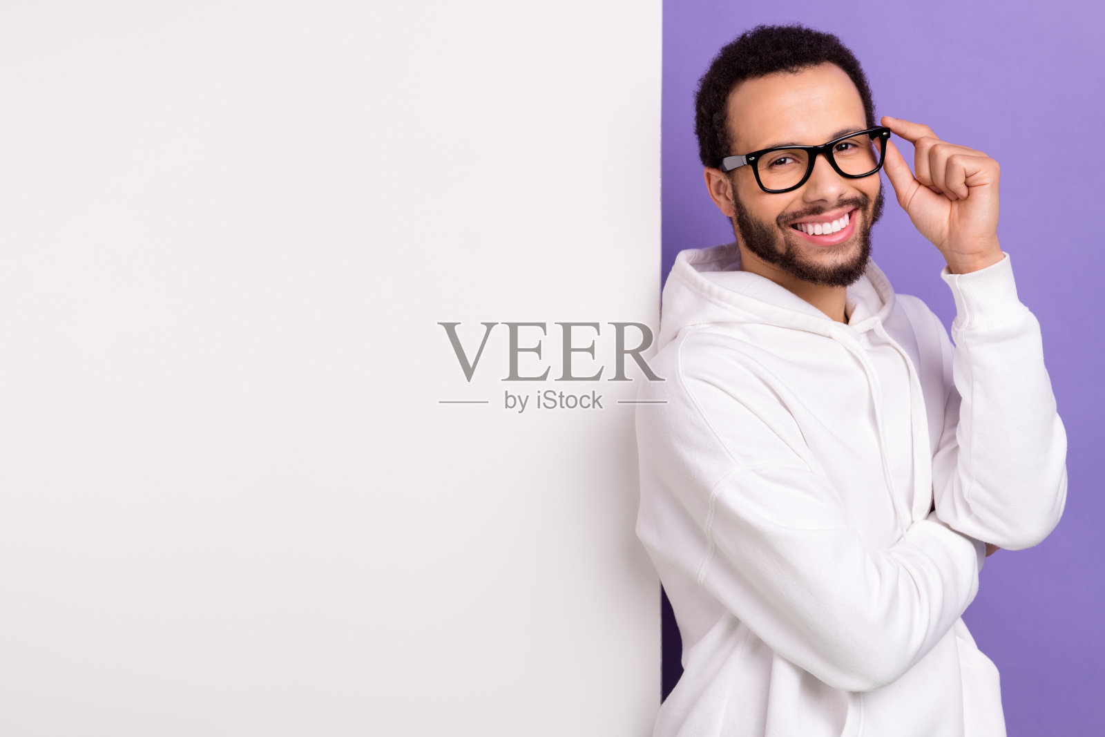 年轻的微笑企业家家伙的照片穿着白色运动衫触摸他的眼镜附近的大横幅空白空间孤立的紫色背景照片摄影图片