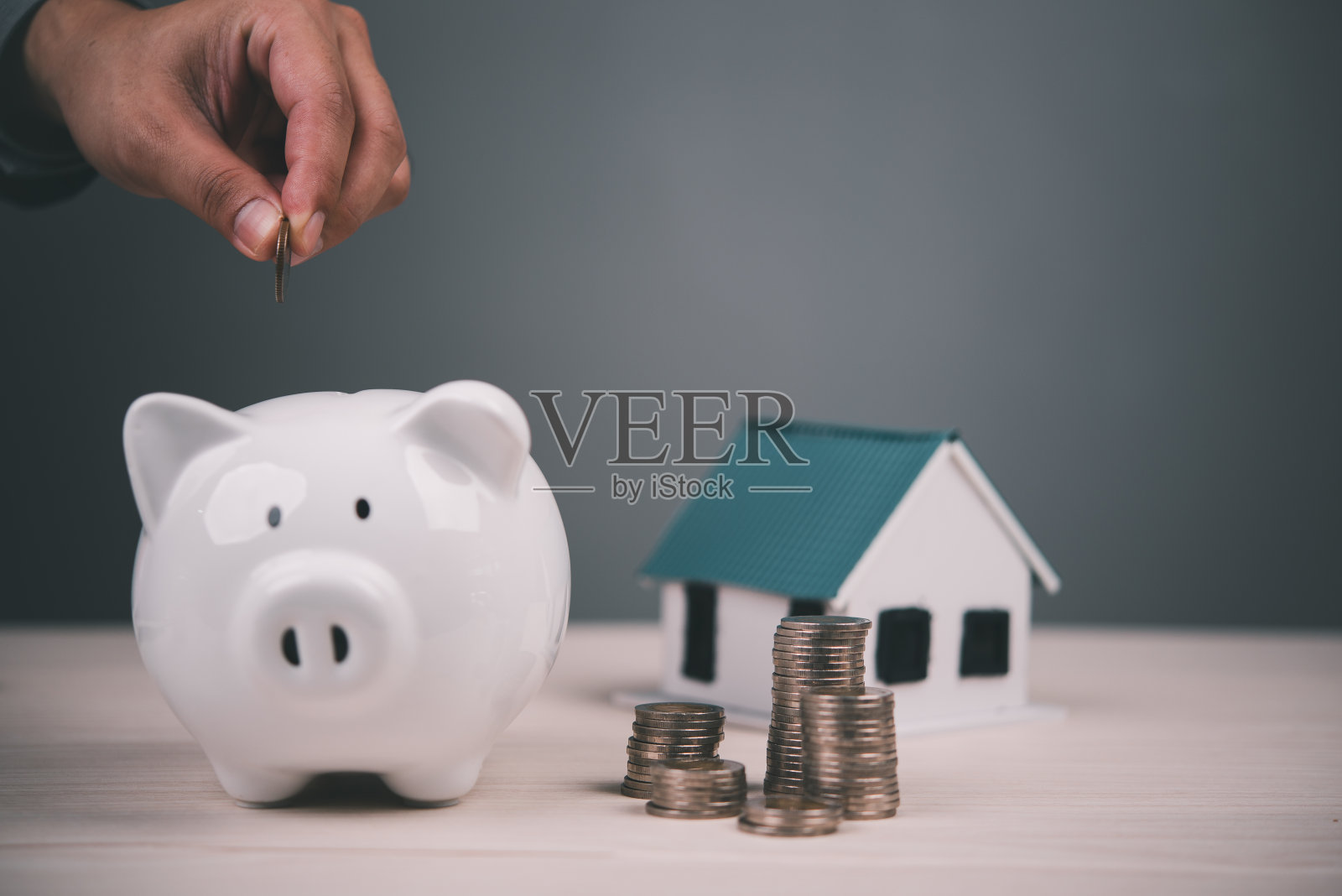 手将硬币放入房子模型和硬币堆旁边的白色储蓄罐。象征储蓄、经济增长和房地产投资。预算、计划和经济管理。照片摄影图片