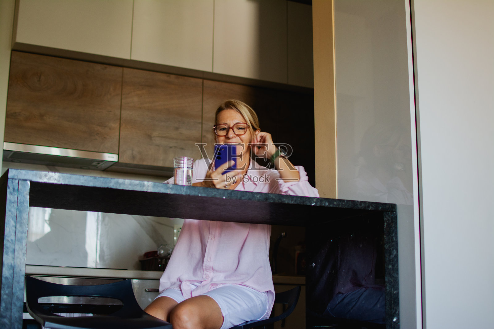 更年期戴着眼镜的成熟金发女人站在厨房里用手机照片摄影图片