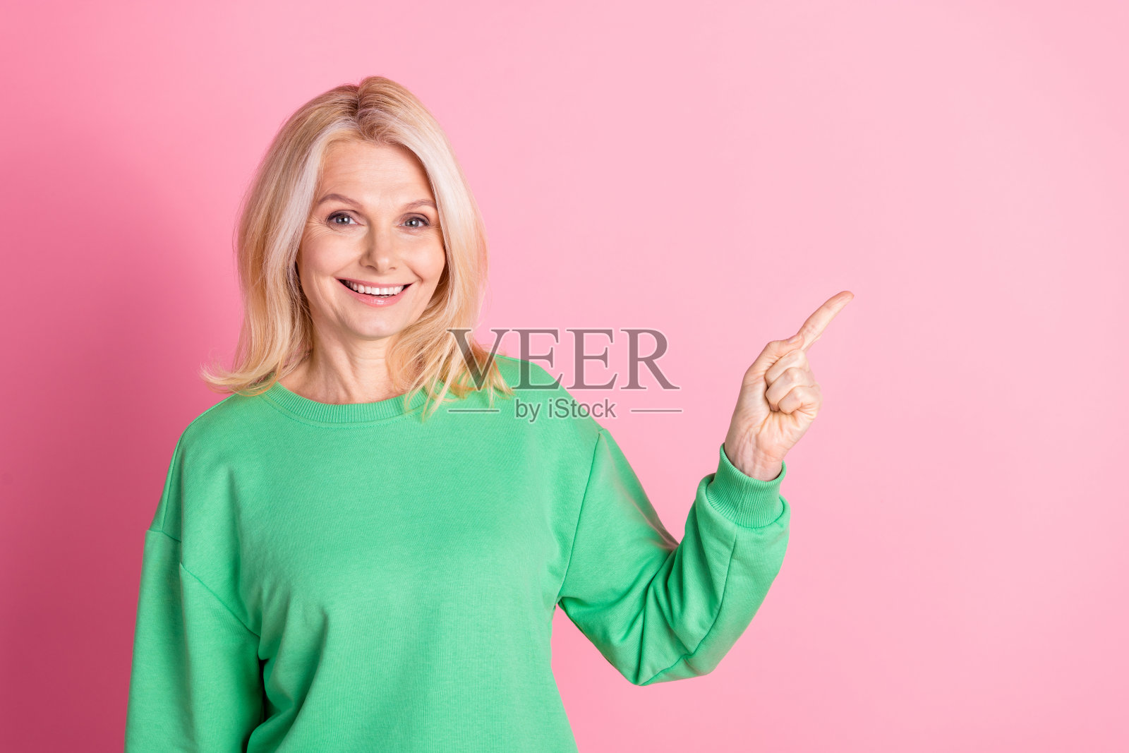 照片中迷人的退休妇女的肖像点空穿着时髦的绿色衣服孤立在粉红色的背景照片摄影图片